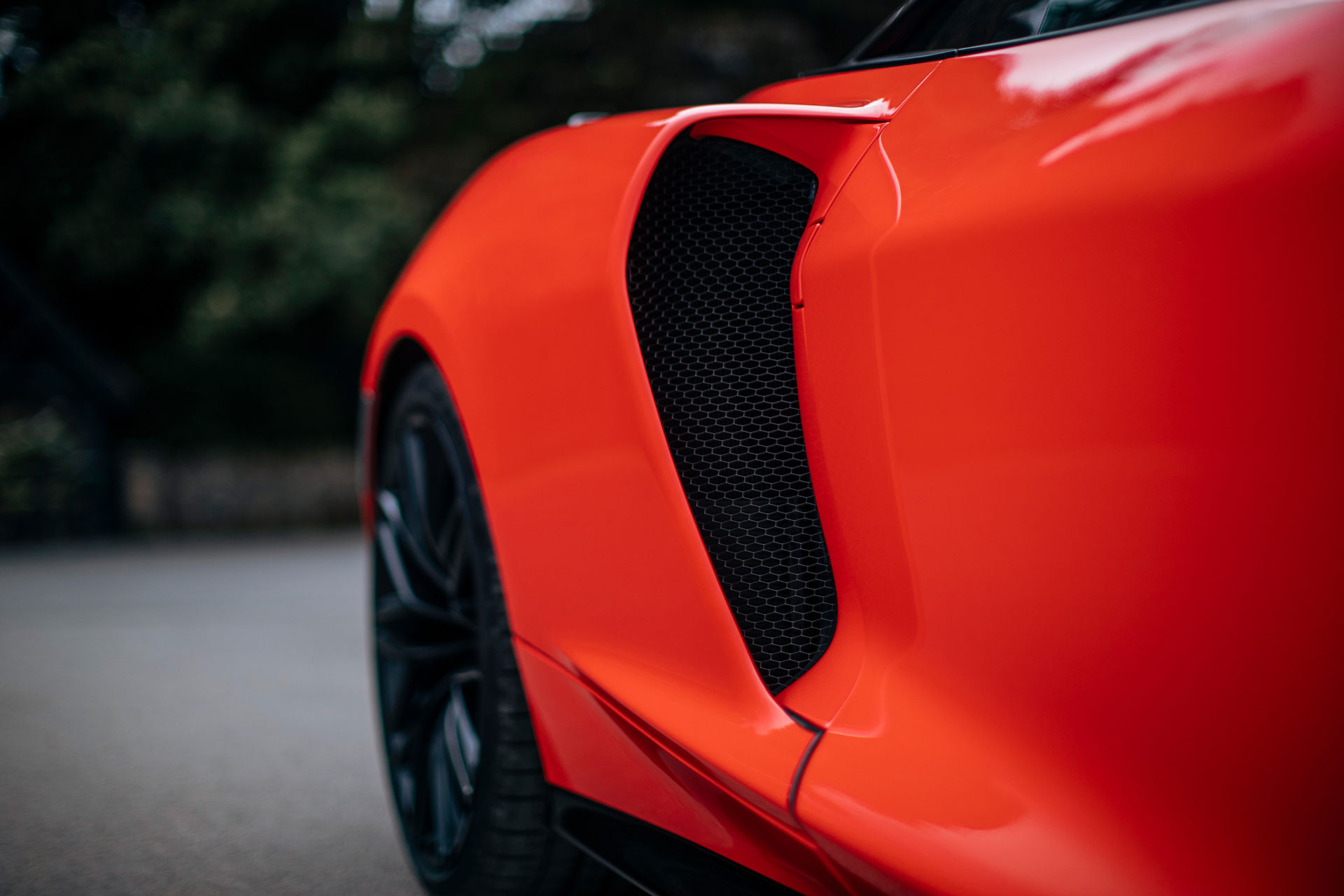 A close-up, low-angle shot highlighting the side air intake and rear wheel of a bright red McLaren GTS.
