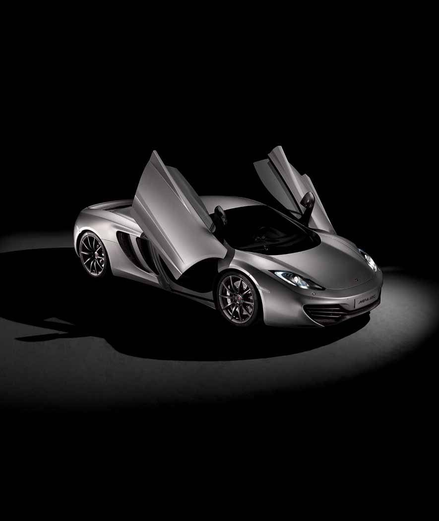 Dark silver McLaren 12C with its dihedral doors open, photographed in a dark dramatic studio environment.