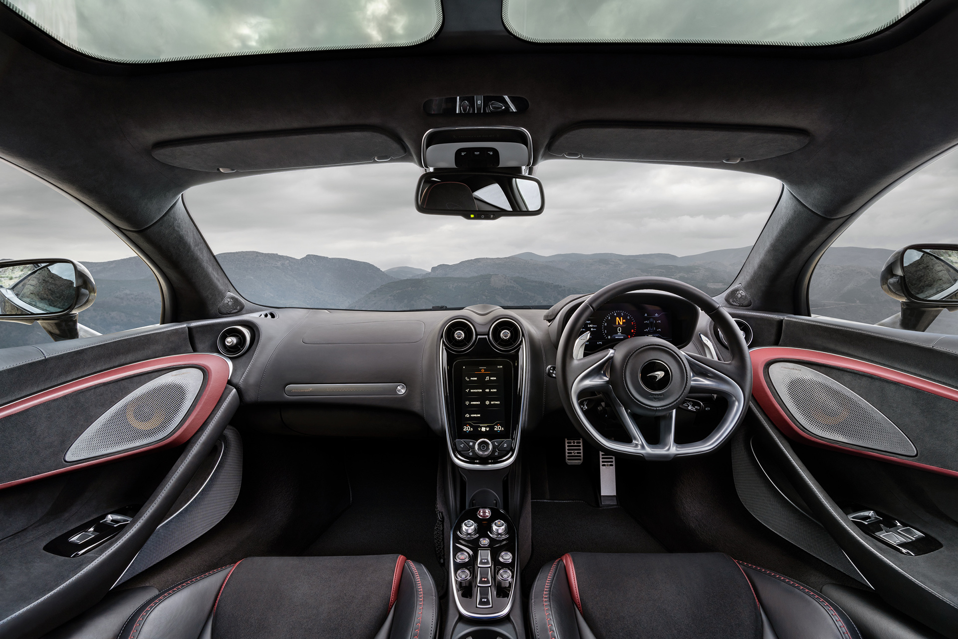 The interior of a McLaren GT, featuring a panoramic roof, black and red leather seats, a digital dashboard, and the centre console with an infotainment screen. 