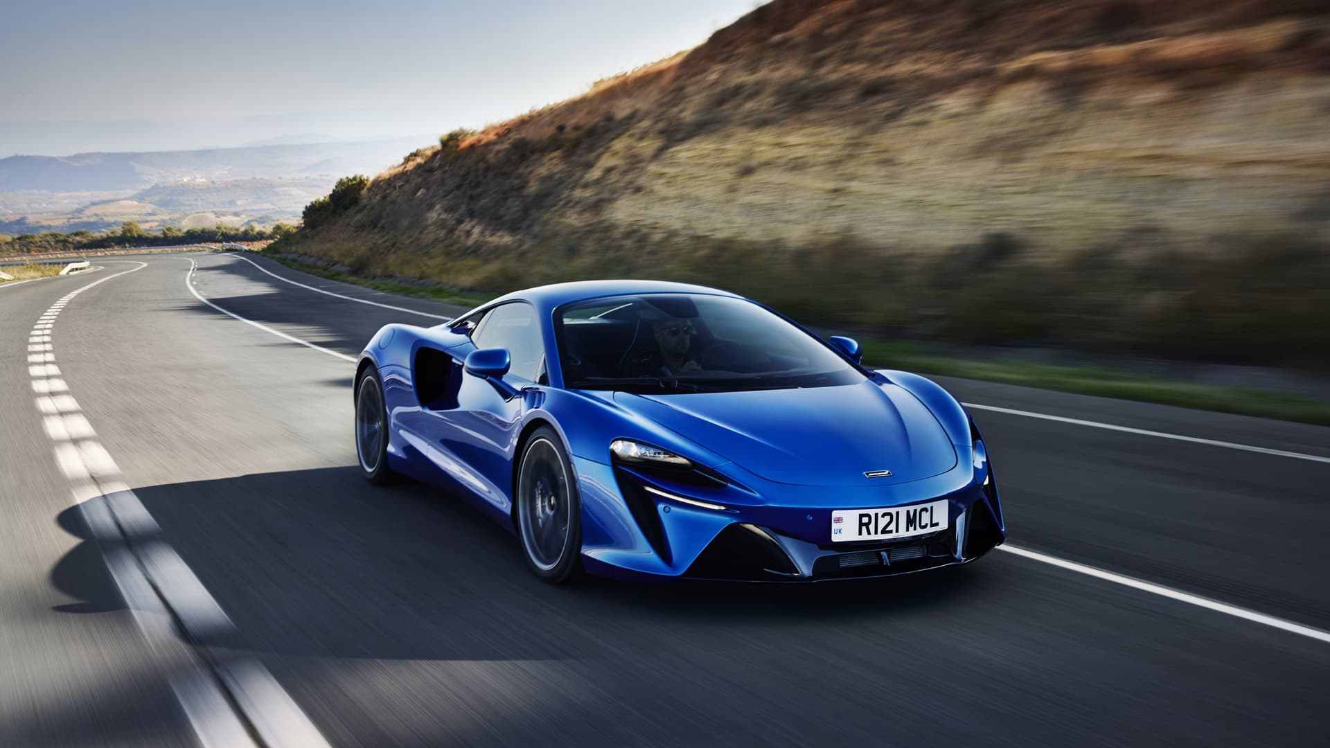 Front left shot of blue McLaren Artura driving on mountain road.