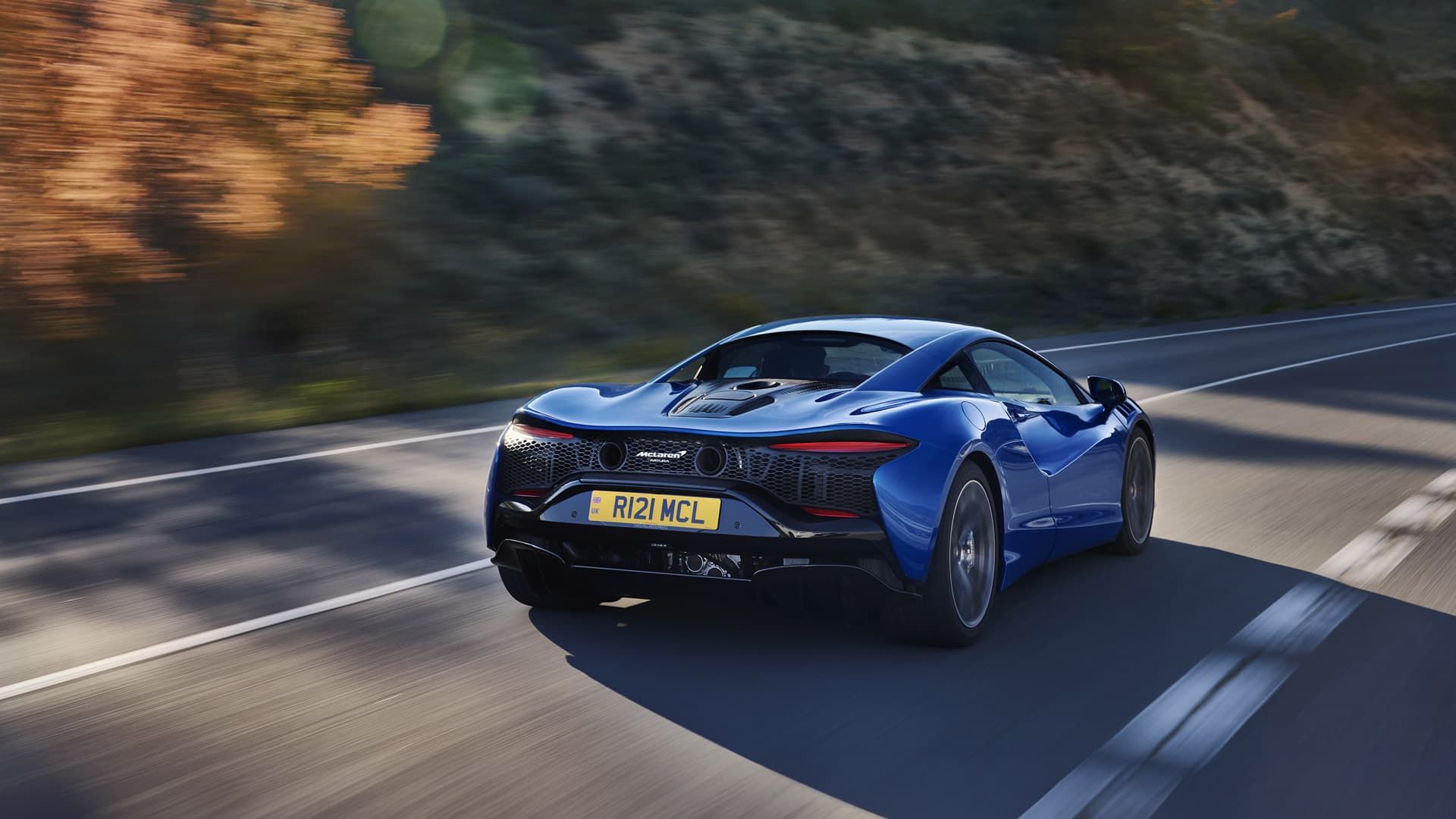 Rear shot of blue McLaren Artura driving on mountain road.
