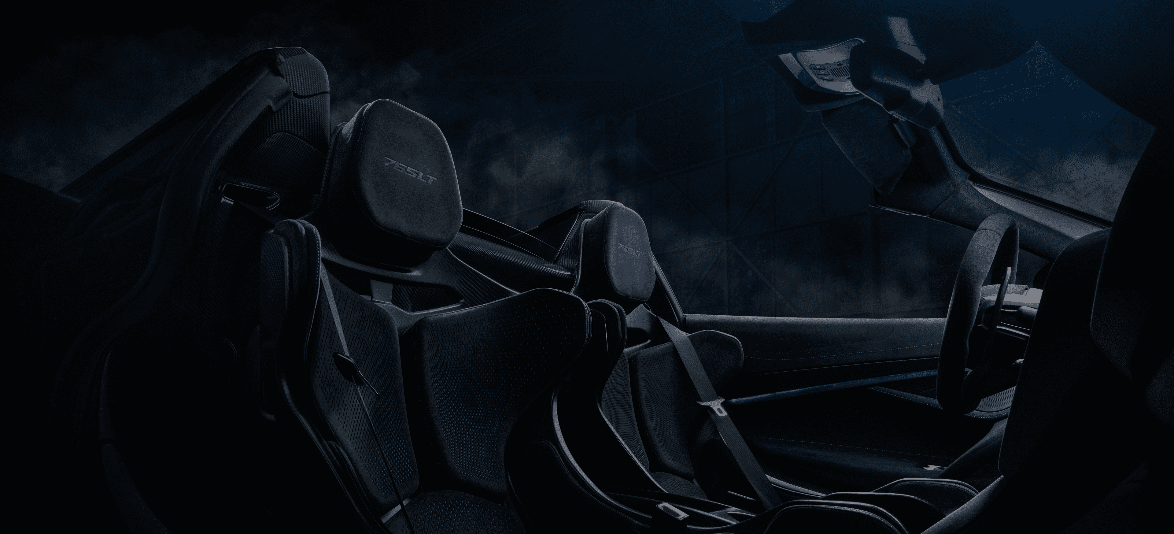 A close-up of the interior of a McLaren 765LT Spider, showing the lightweight, black carbon fiber racing seats with '765LT' embroidered on the headrests.