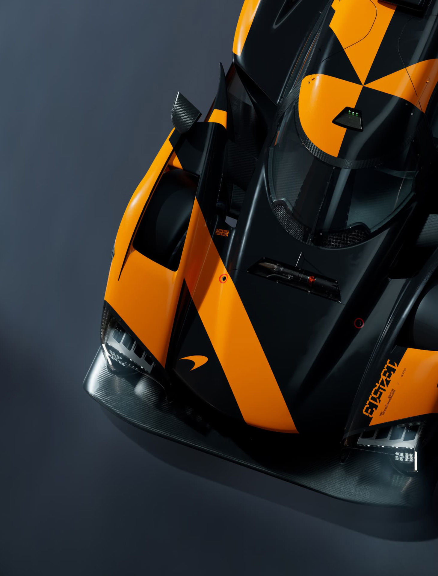 An abstract top-down view of a black and orange McLaren endurance race car prototype, showcasing its unique livery and carbon fiber bodywork.