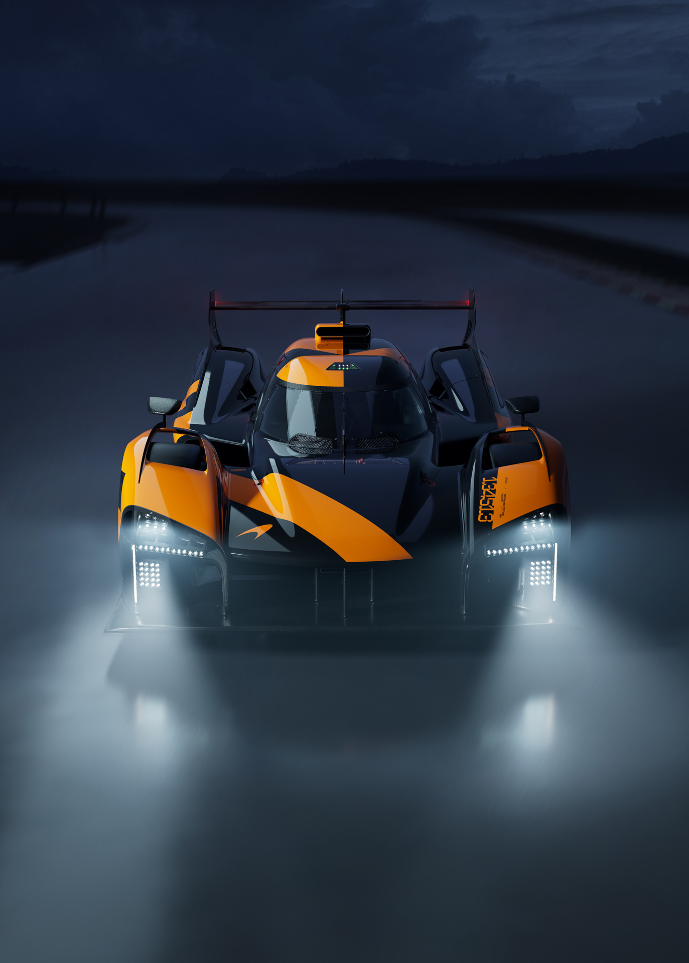 A striking front view of a black and orange McLaren endurance race car prototype at night, with its bright LED headlights illuminated.