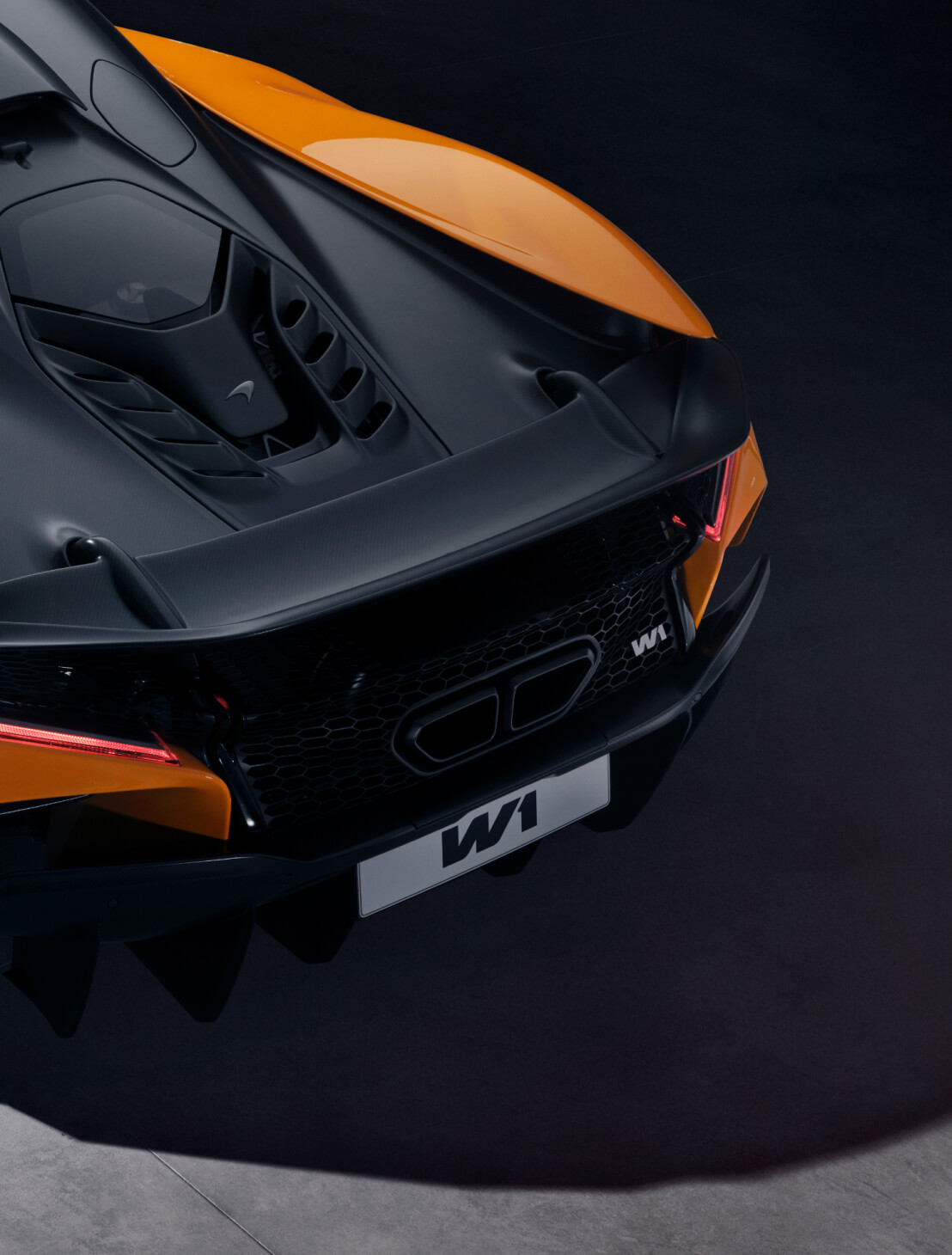 A black rear deck on an orange McLaren W1 in a dark shadowed environment.