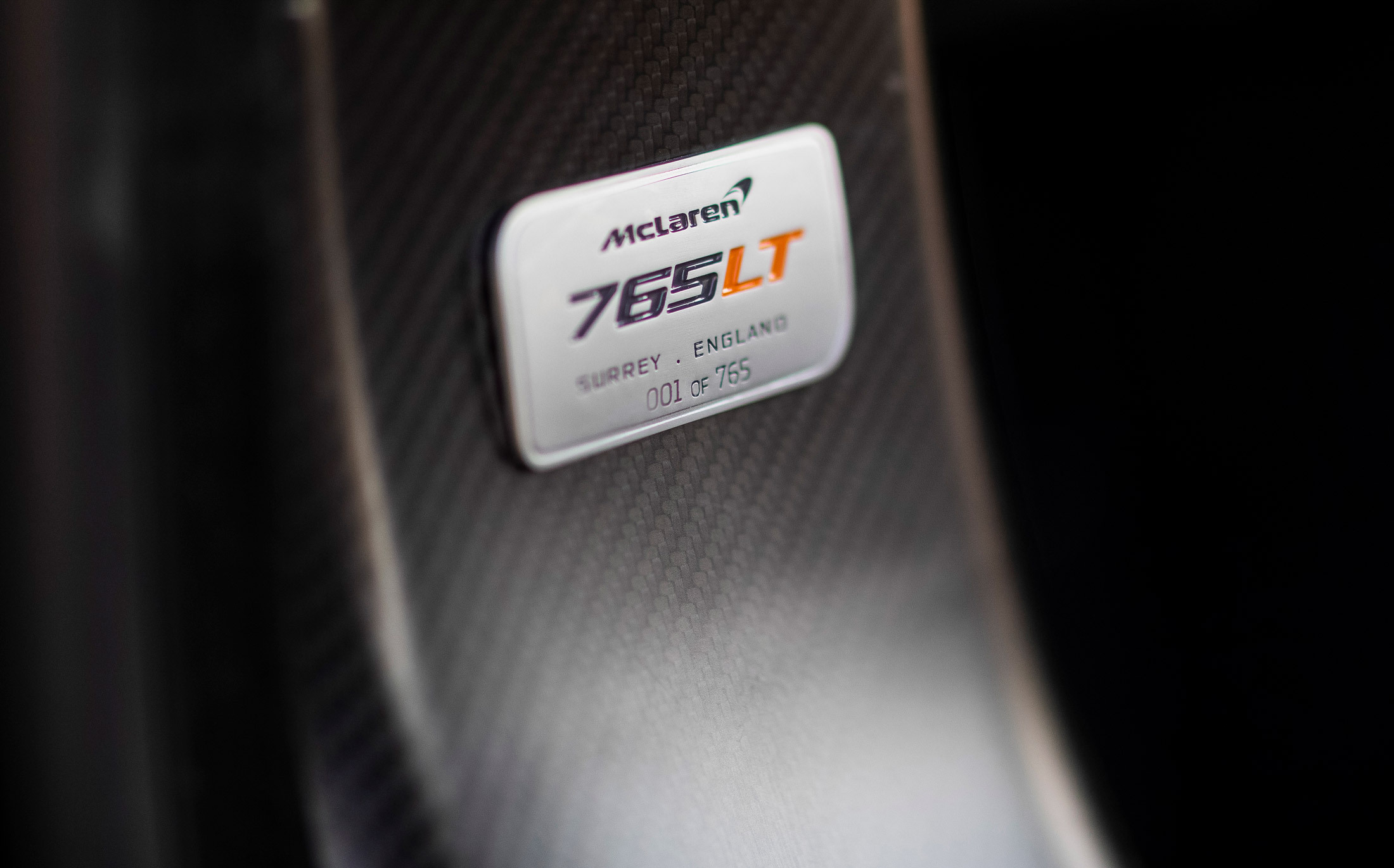 McLaren 765LT nameplate on carbon fiber panel, engraved with '001 of 765, highlighting its limited production and exclusivity