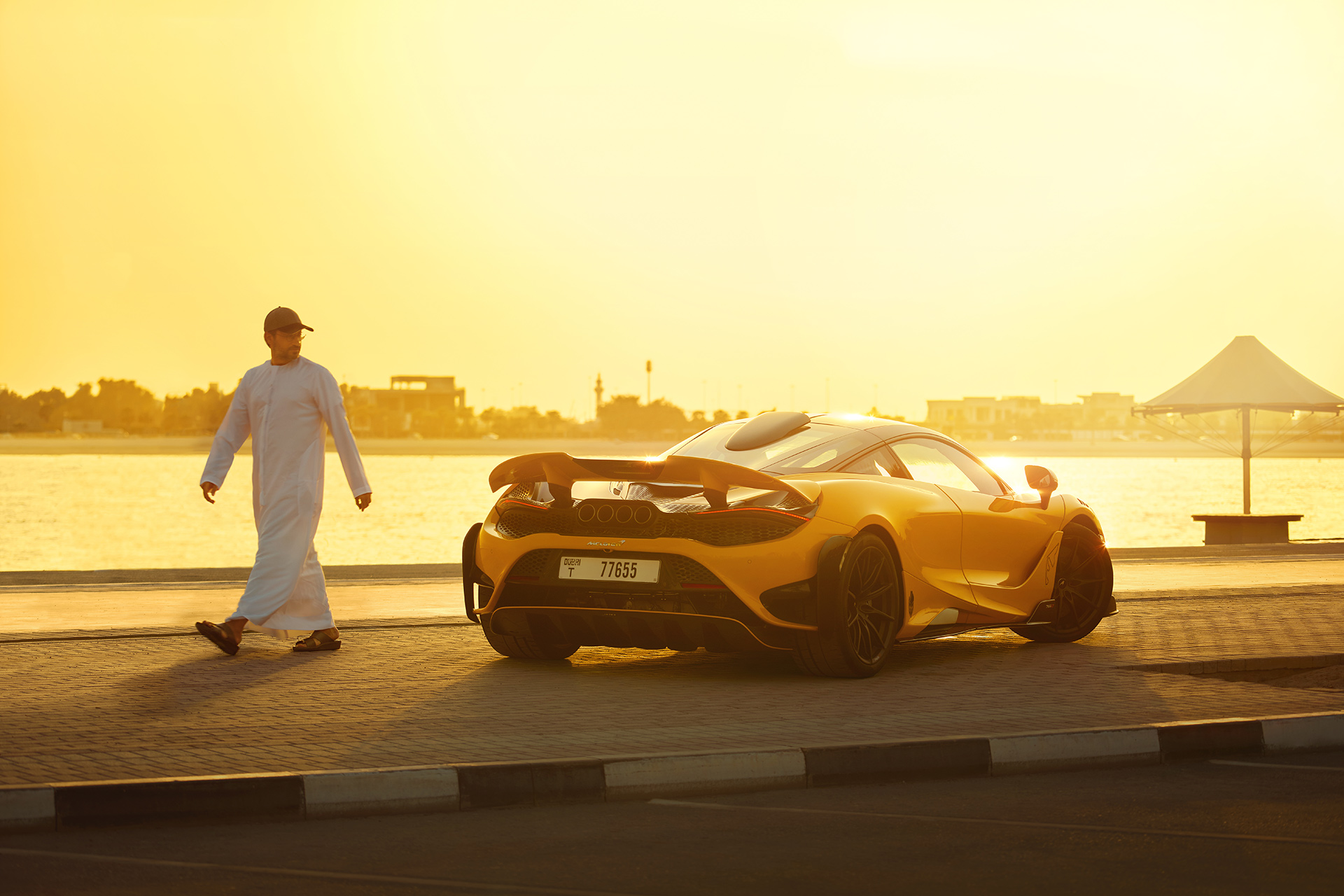 Man standing beside yellow McLaren supercar at sunset, representing LT community and passion.