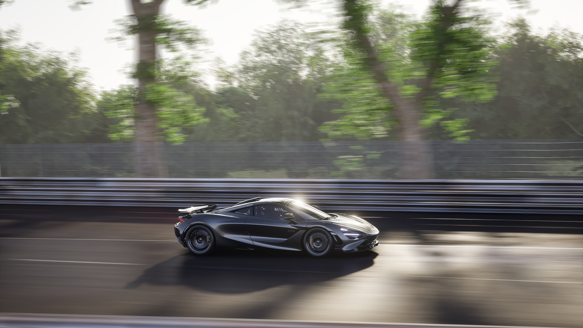 A side-profile shot of a dark grey McLaren 750S Le Mans edition, speeding down a racetrack with a sun flare and motion blur from the trees in the background.