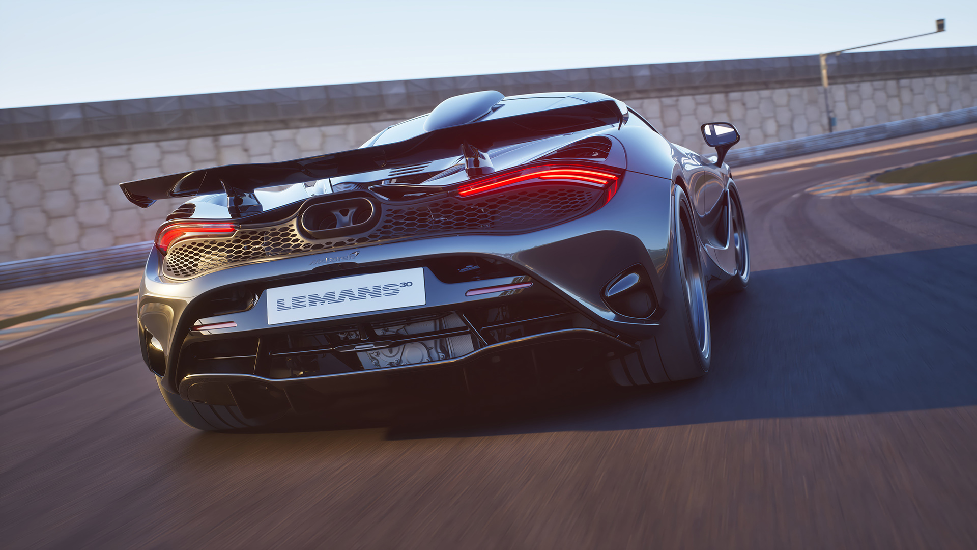 A dynamic rear-three-quarter view of a dark grey McLaren 750S Le Mans special edition on a racetrack, highlighting its aggressive rear design and glowing taillight