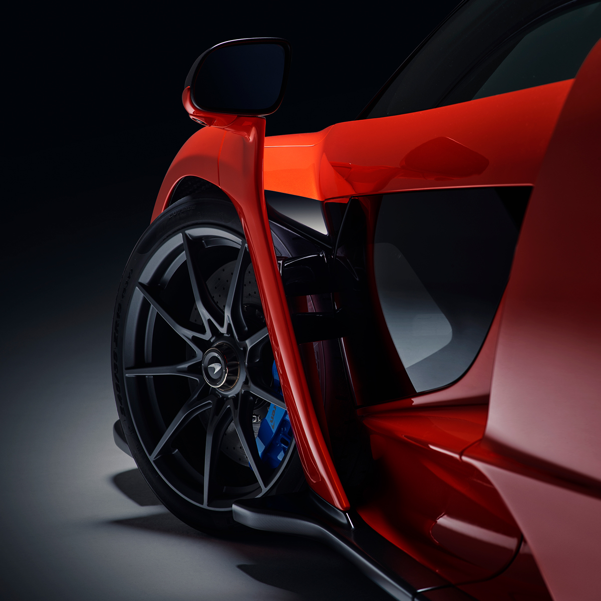 Close up detail of the wheel and body on the side of a red McLaren Senna, photographed in a moody studio environment.