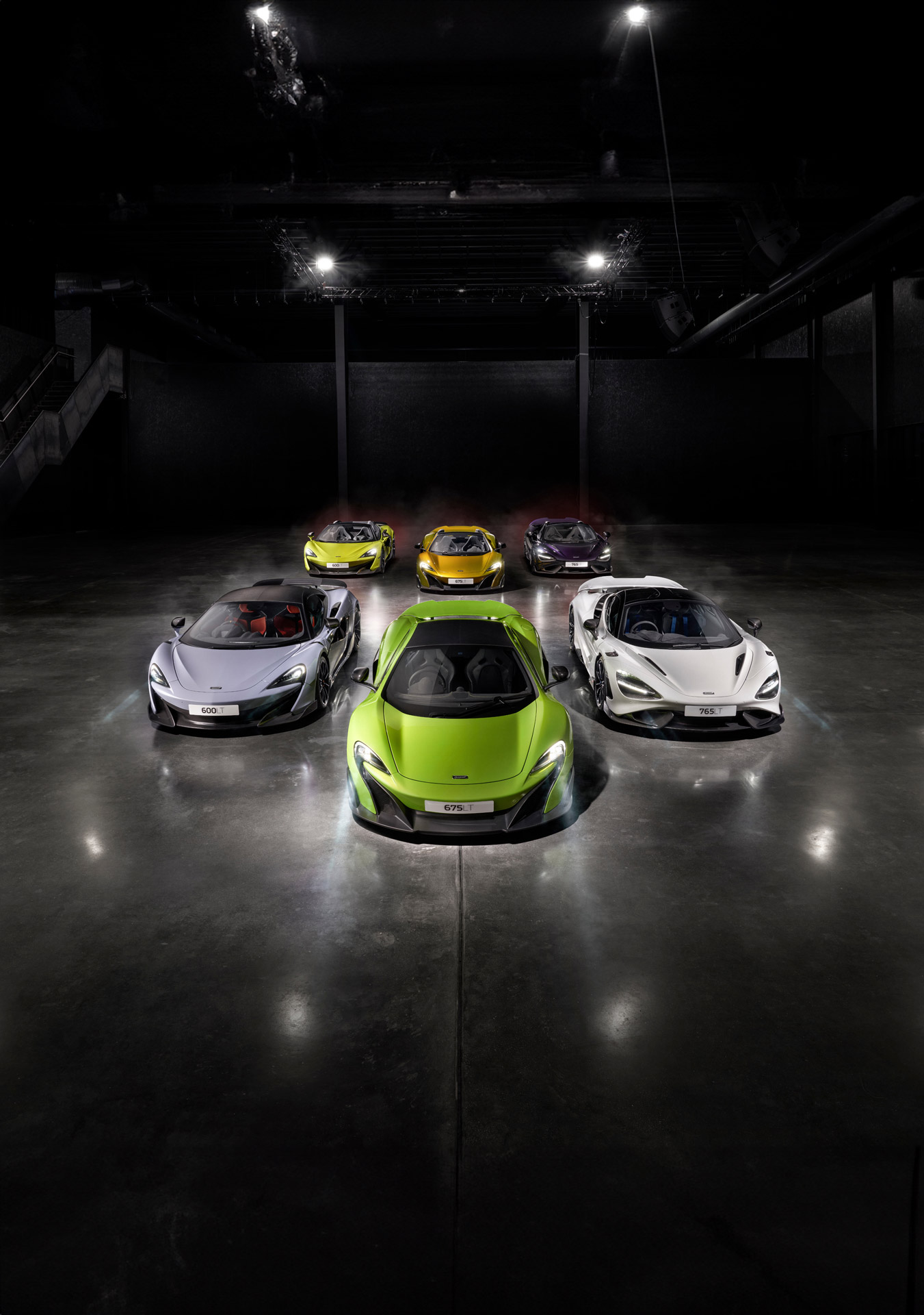 A lineup of McLaren Longtail cars, featuring the 675LT in green, 600LT in grey, and 765LT in white, in a dramatic studio shot.