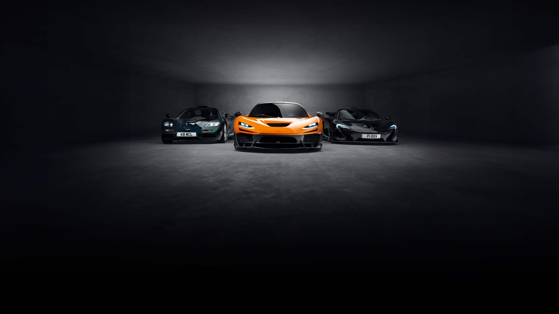 Three McLaren supercars in a dark studio: a McLaren F1, an orange W1, and a P1.