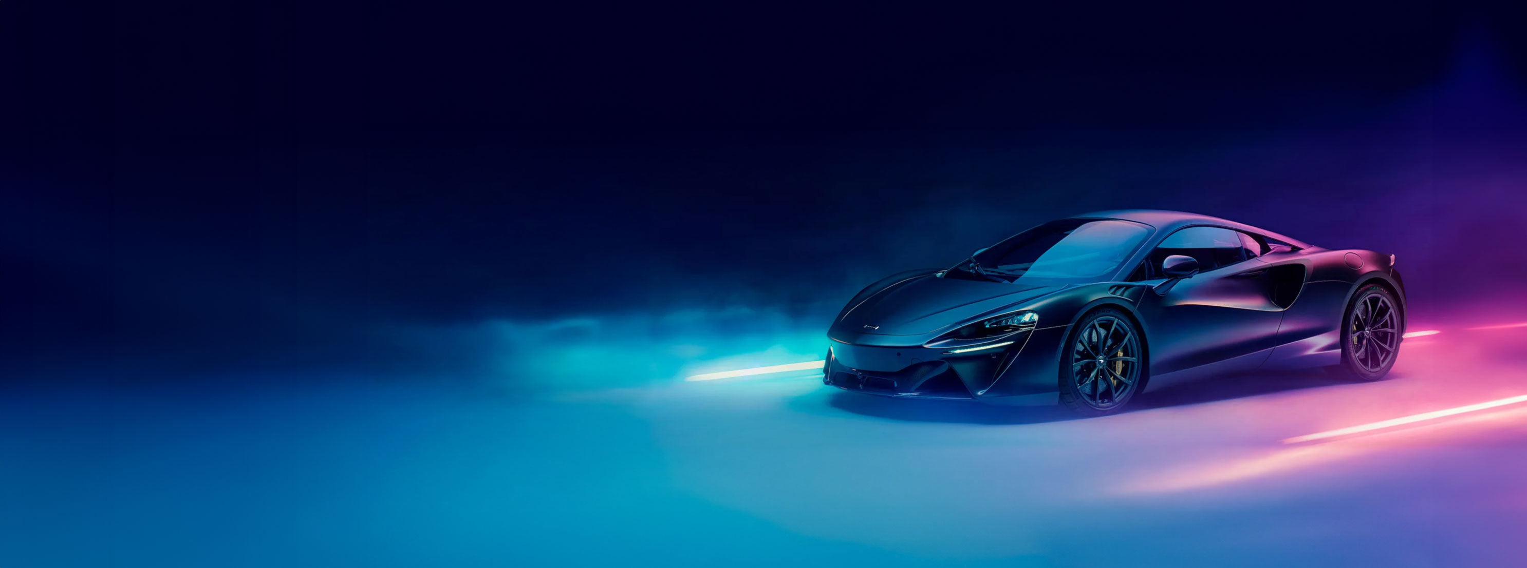 A dark, sleek McLaren Artura sports car positioned on the right side of the frame, bathed in vibrant blue and pink neon lighting with smoke effects, creating a dramatic atmosphere.