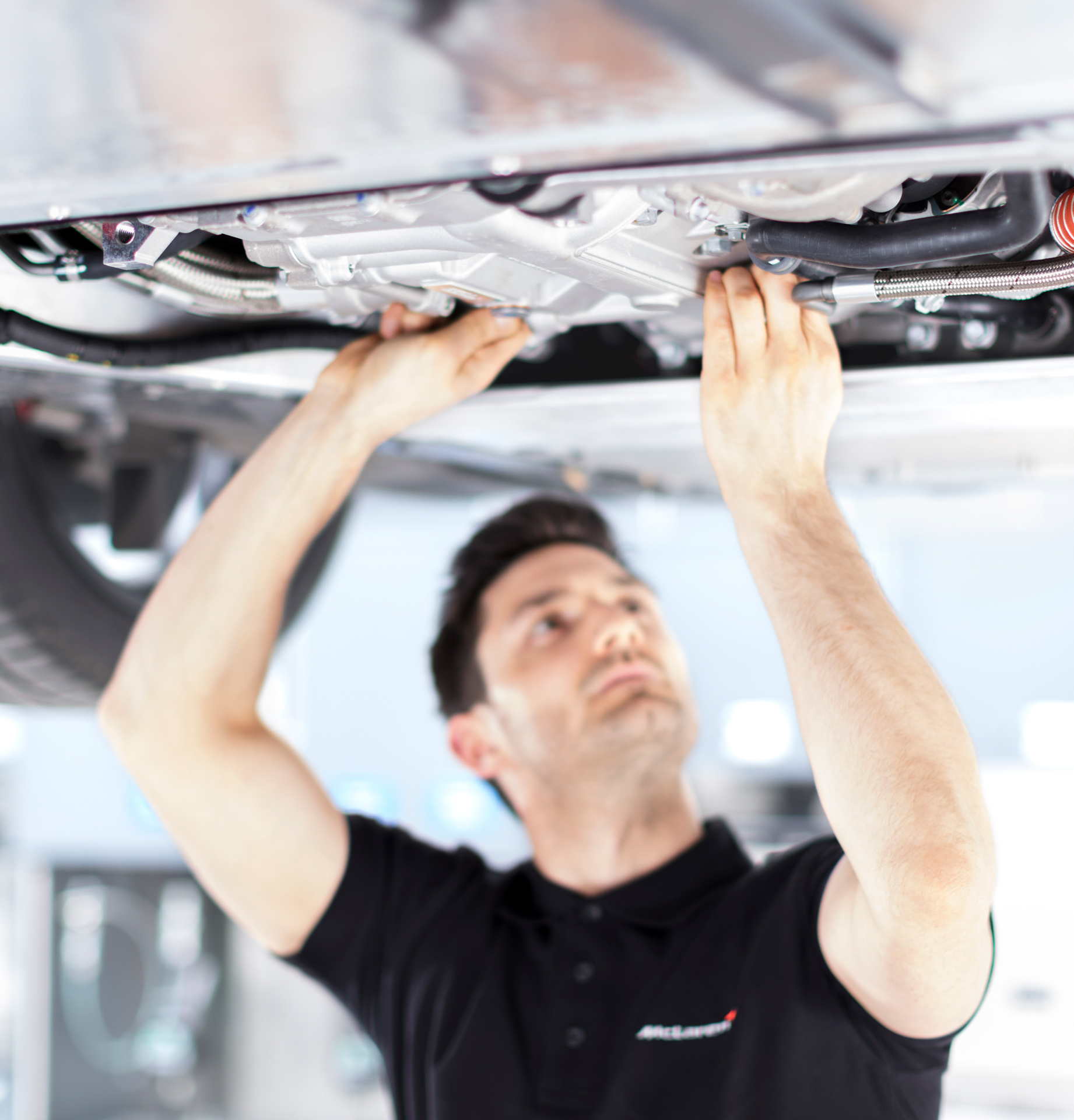 A McLaren specialist working on the underside of a car, demonstrating the rigorous pre-owned inspection process.