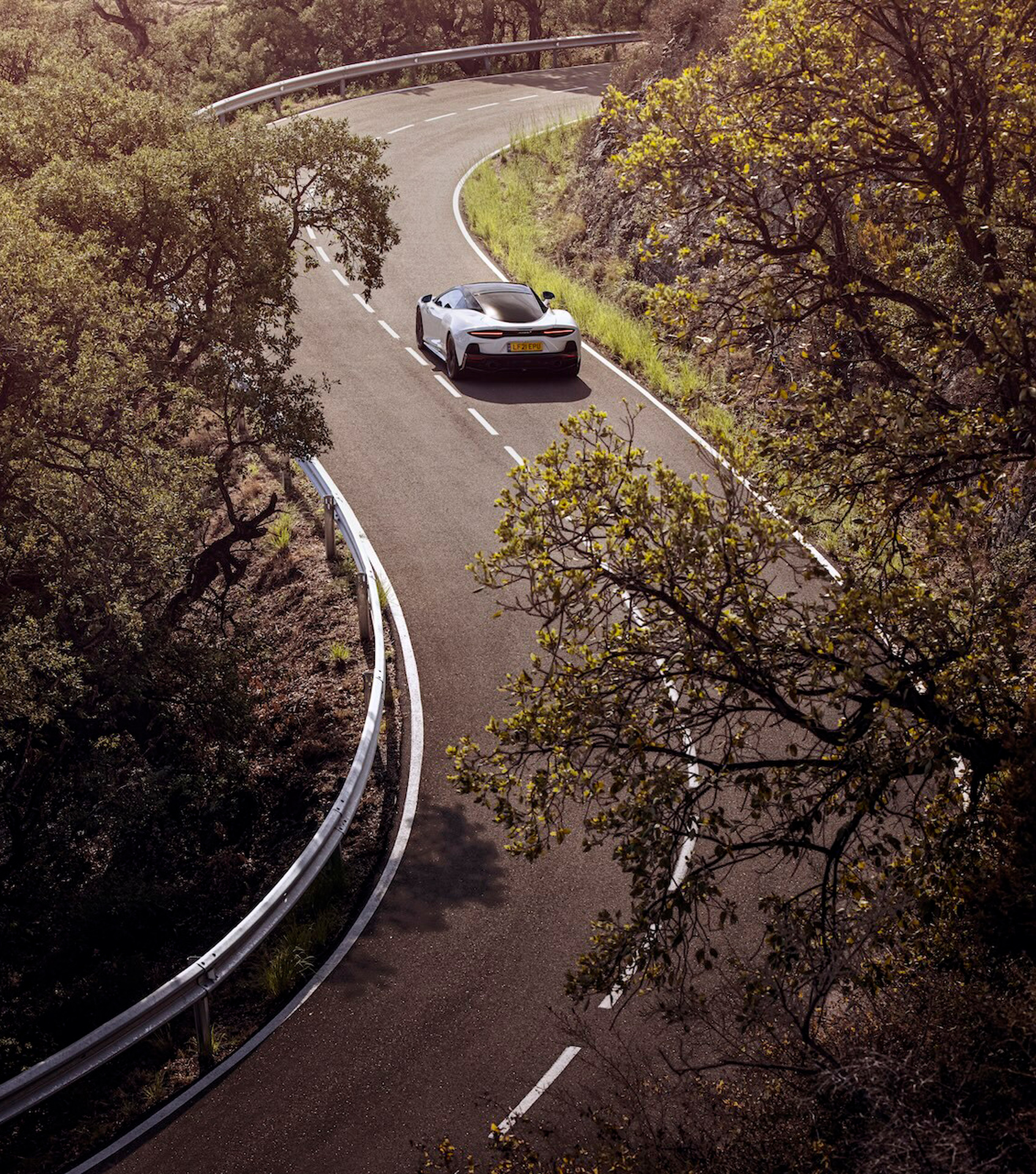 An aerial view of a white McLaren Artura on a twisting road, highlighting the peace of mind provided by a qualified warranty.