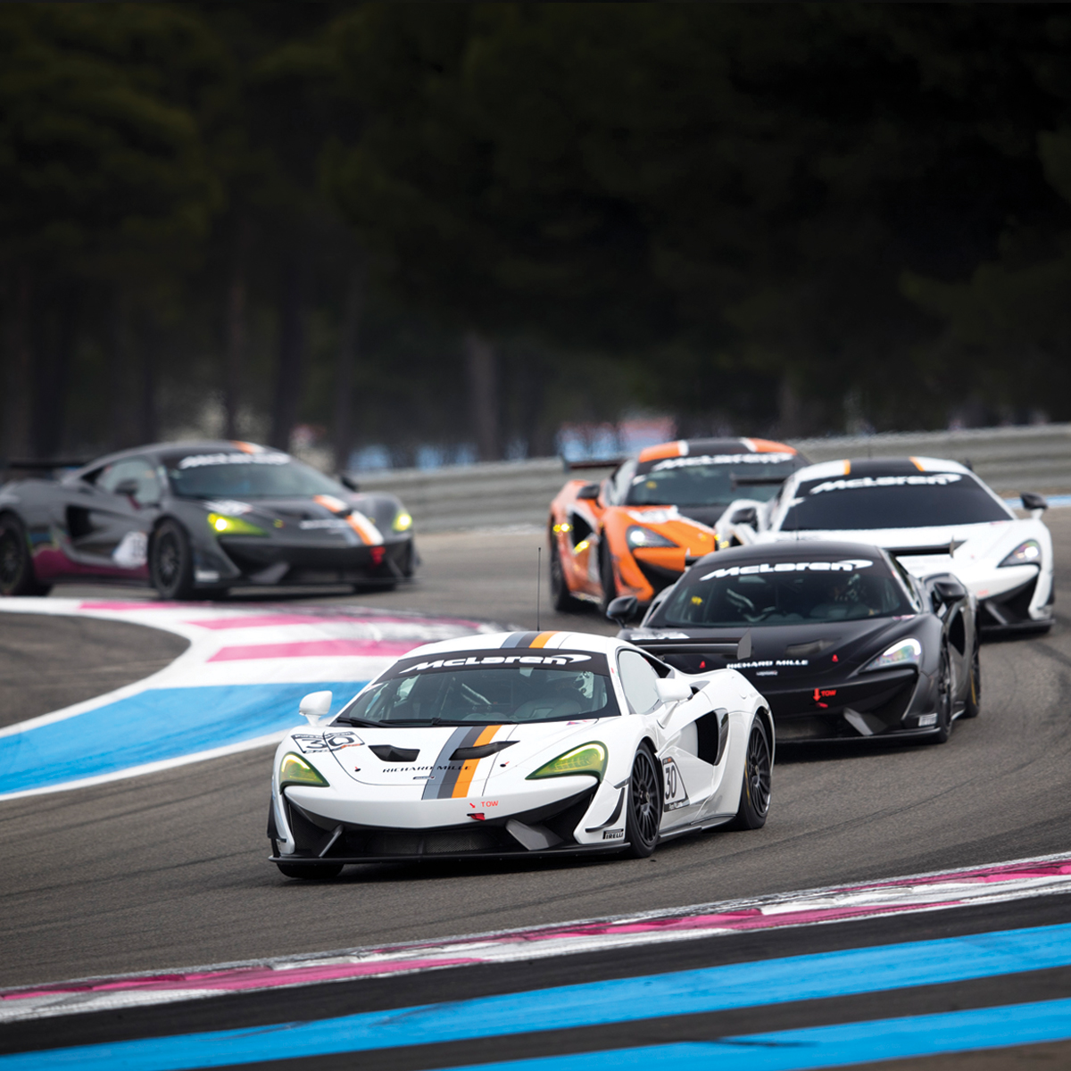 Series of McLaren cars driving around a race track. 