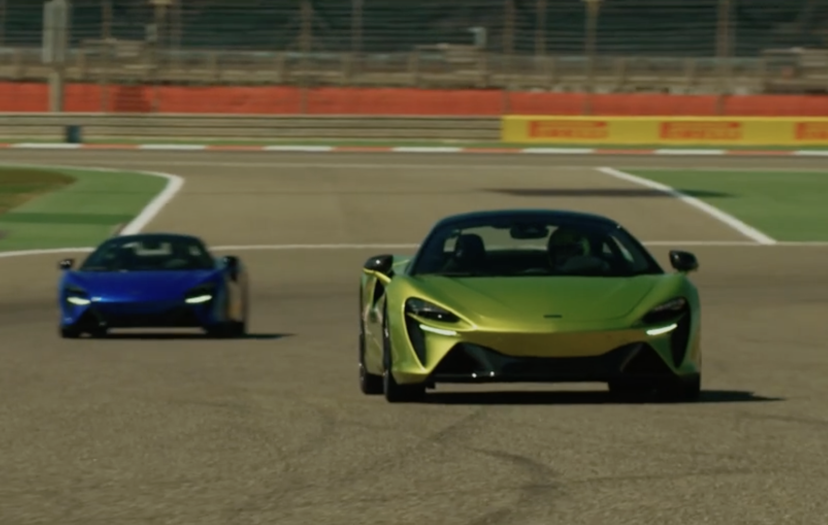 Lando Norris driving a green McLaren Artura on a race track and Oscar Piastri driving behind in a blue artura.