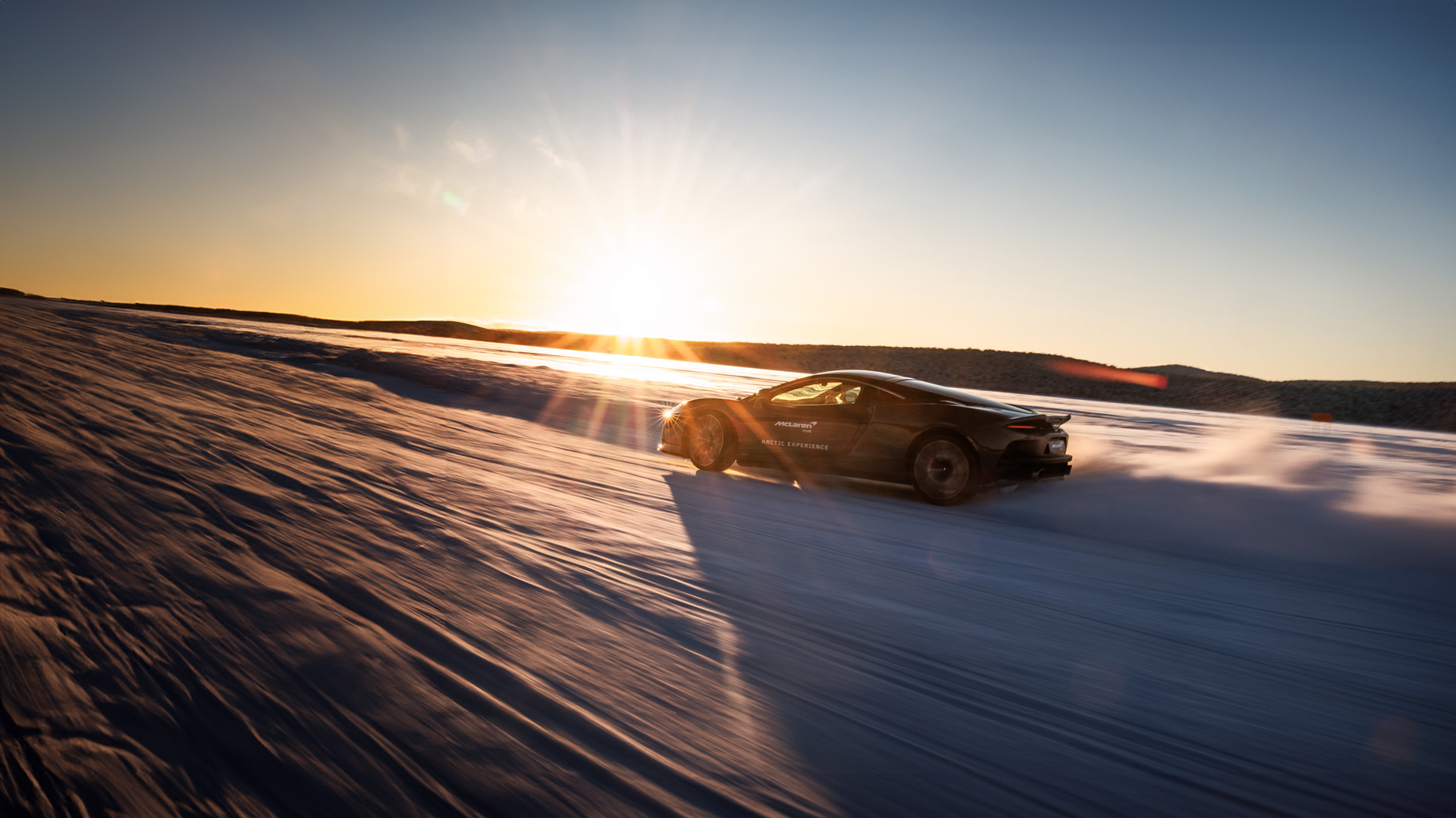 A dark McLaren supercar driving at high speed on a vast, snow-covered landscape during an Arctic driving experience.