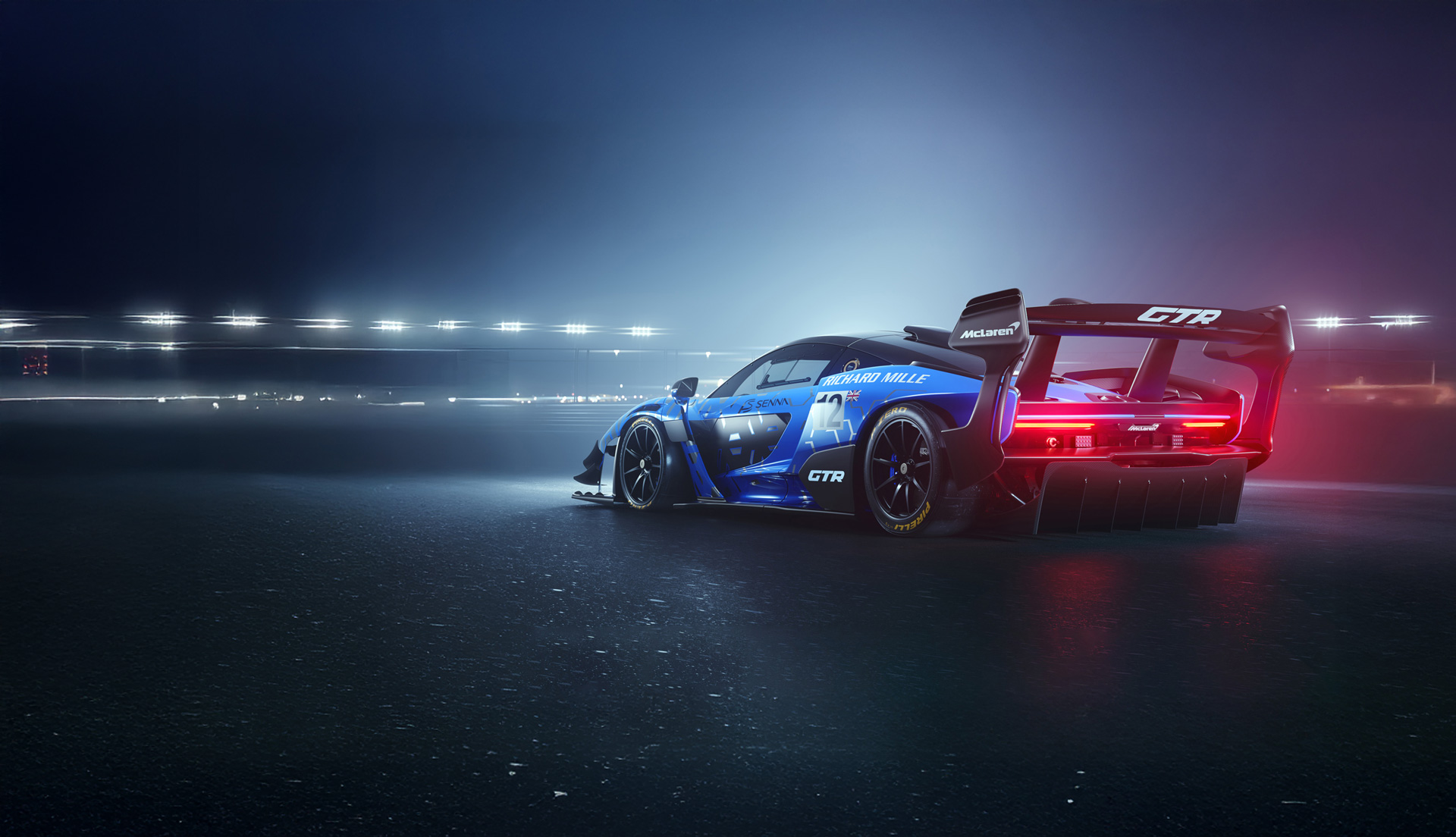 A blue patterned McLaren Senna GTR parked in an urban setting at night, under street lights. 