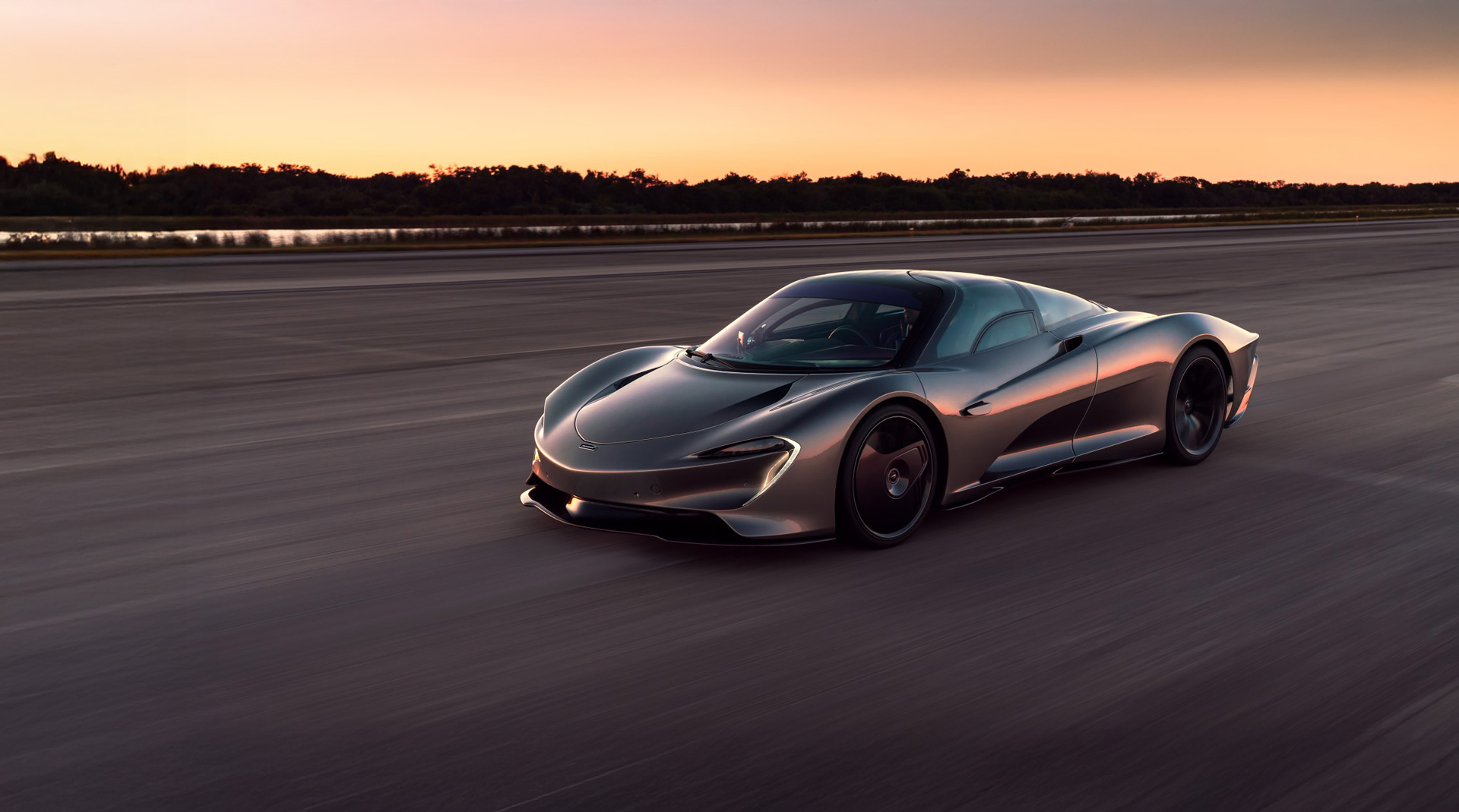 Lower rear side view of a grey McLaren Speedtail rear as the car drives down a road at speed during sunset.