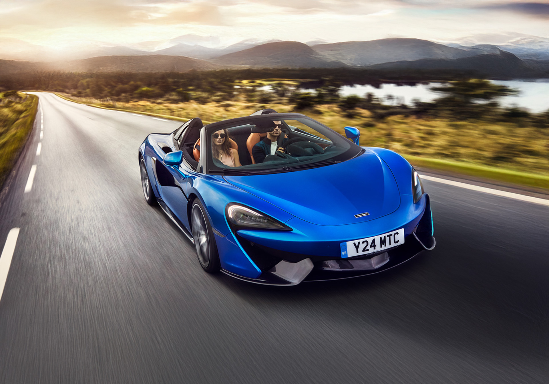 Front view of a blue McLaren 570S Spider, driven by a man, accompanied by a woman sat in the passenger seat.