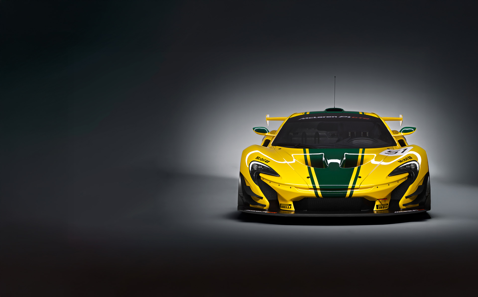 Forward facing yellow McLaren P1 GTR with green racing stripe, number 51, and sponsorship advertising on the body, photographed in a grey studio environment.