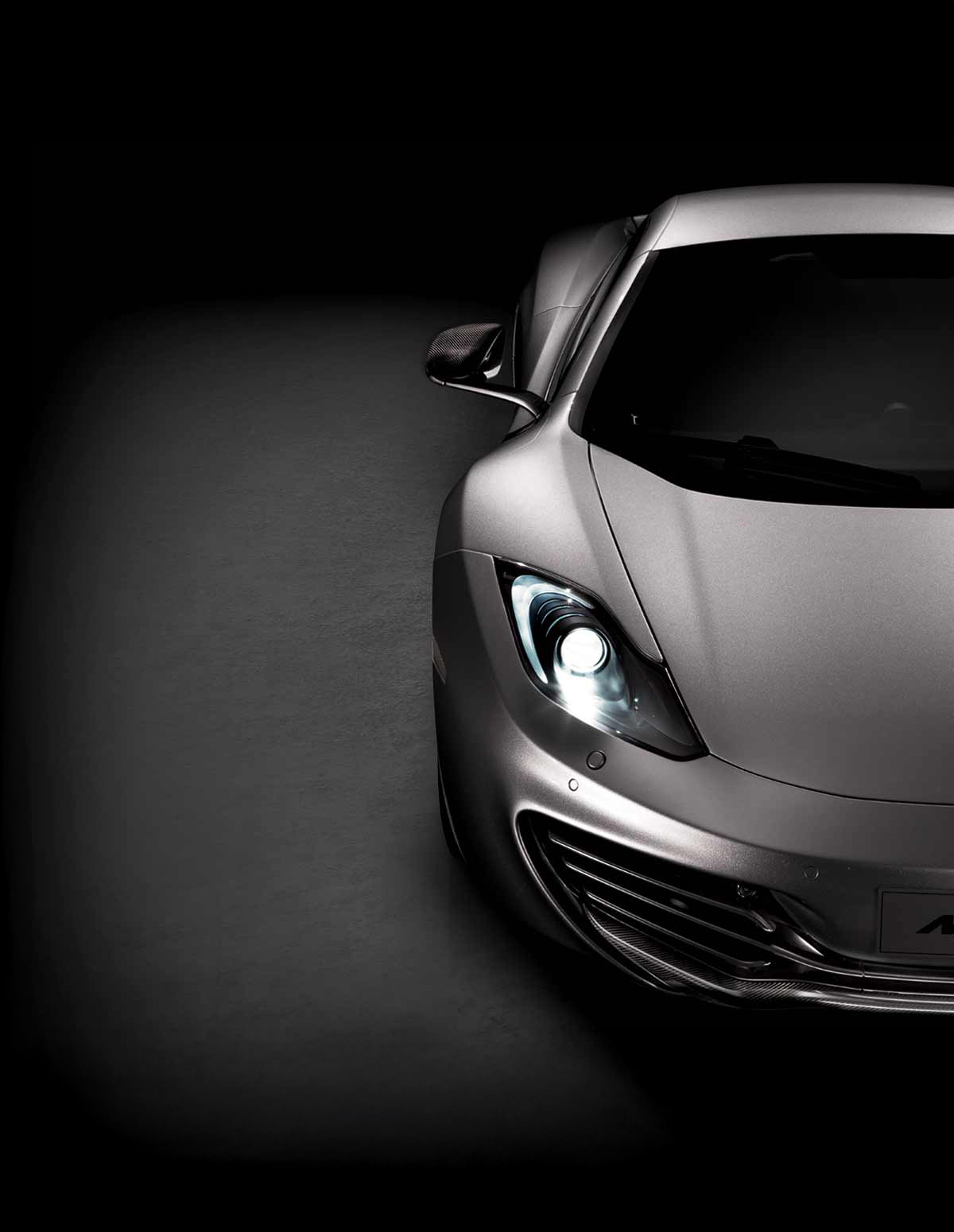 Front view of half a dark silver McLaren 12C, photographed in a dark dramatic studio environment.