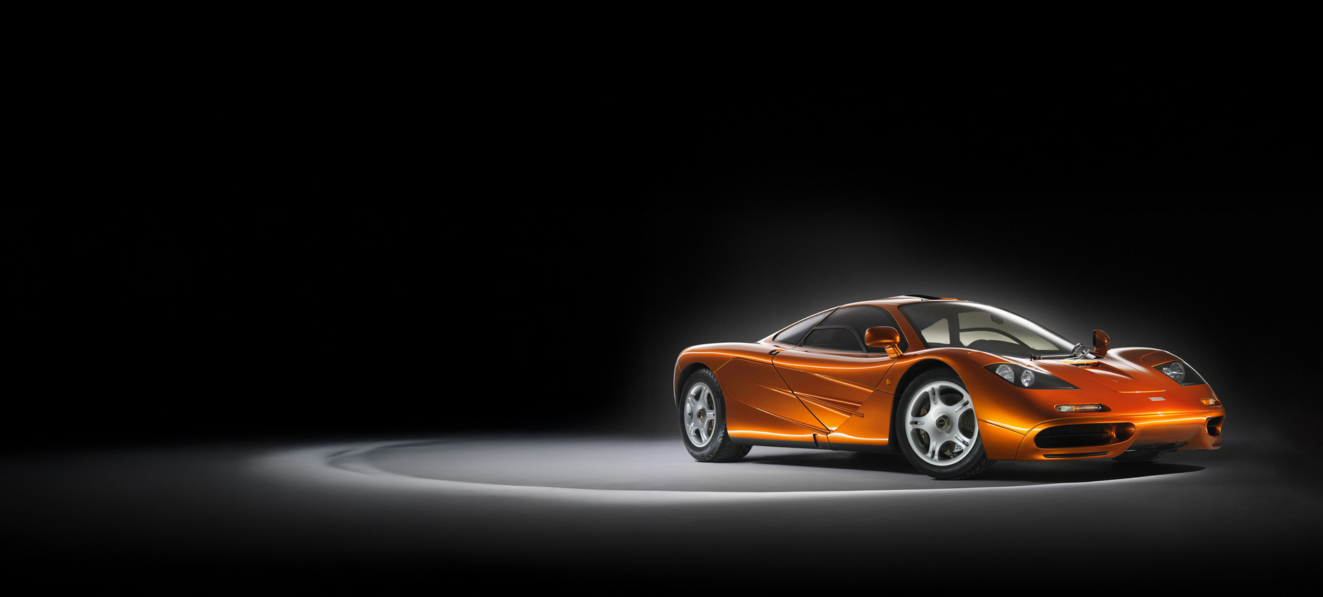 A metallic orange McLaren F1 photographed in a dark studio environment.