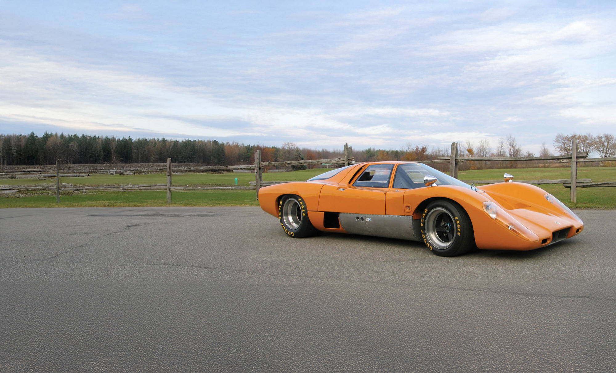 An orange McLaren M6GT parked in a rural location. 