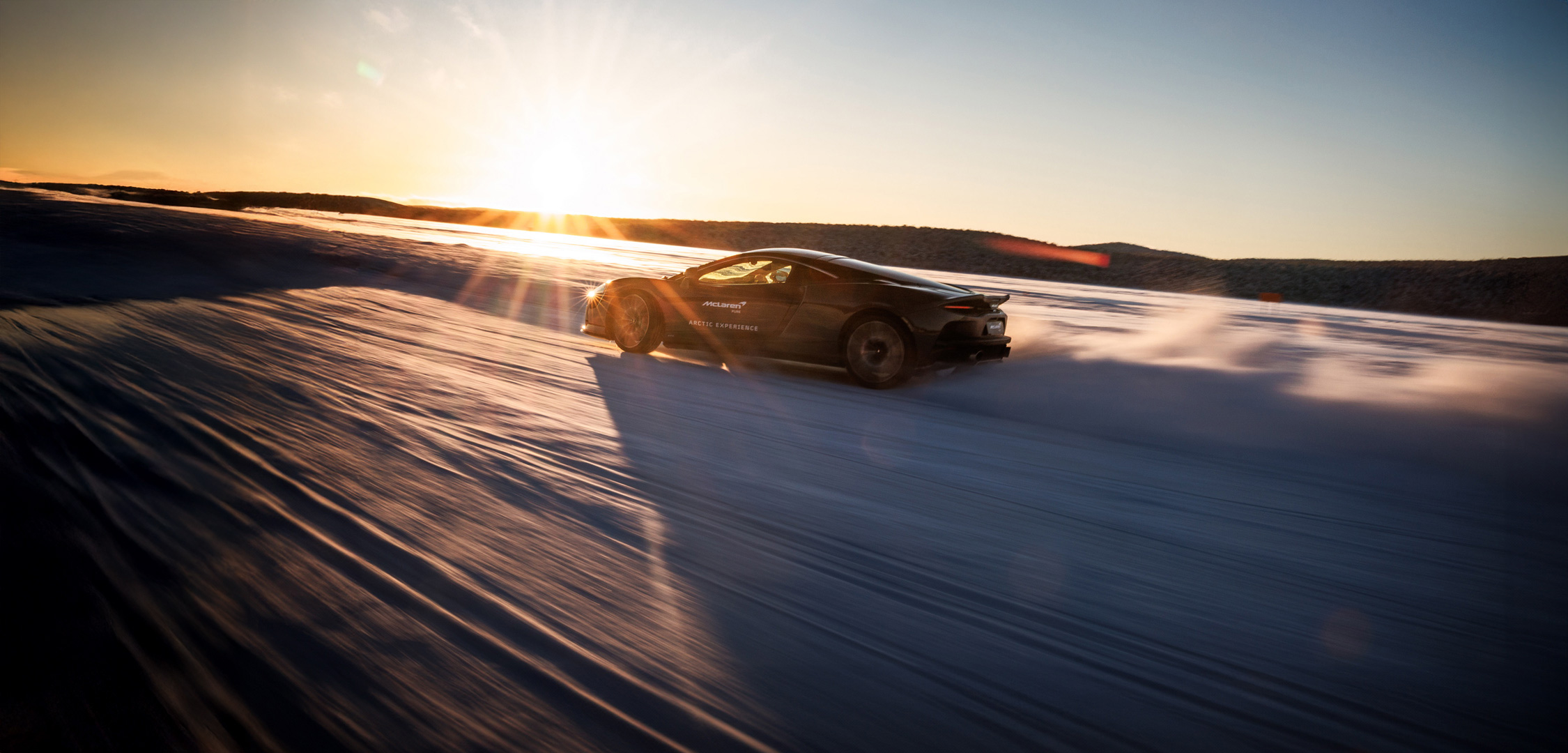 The McLaren GT supercar driving on a vast, snow-covered landscape during an Arctic driving experience.