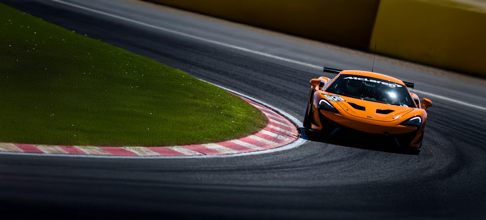 Orange McLaren 570S GT4 driving around a track at speed.