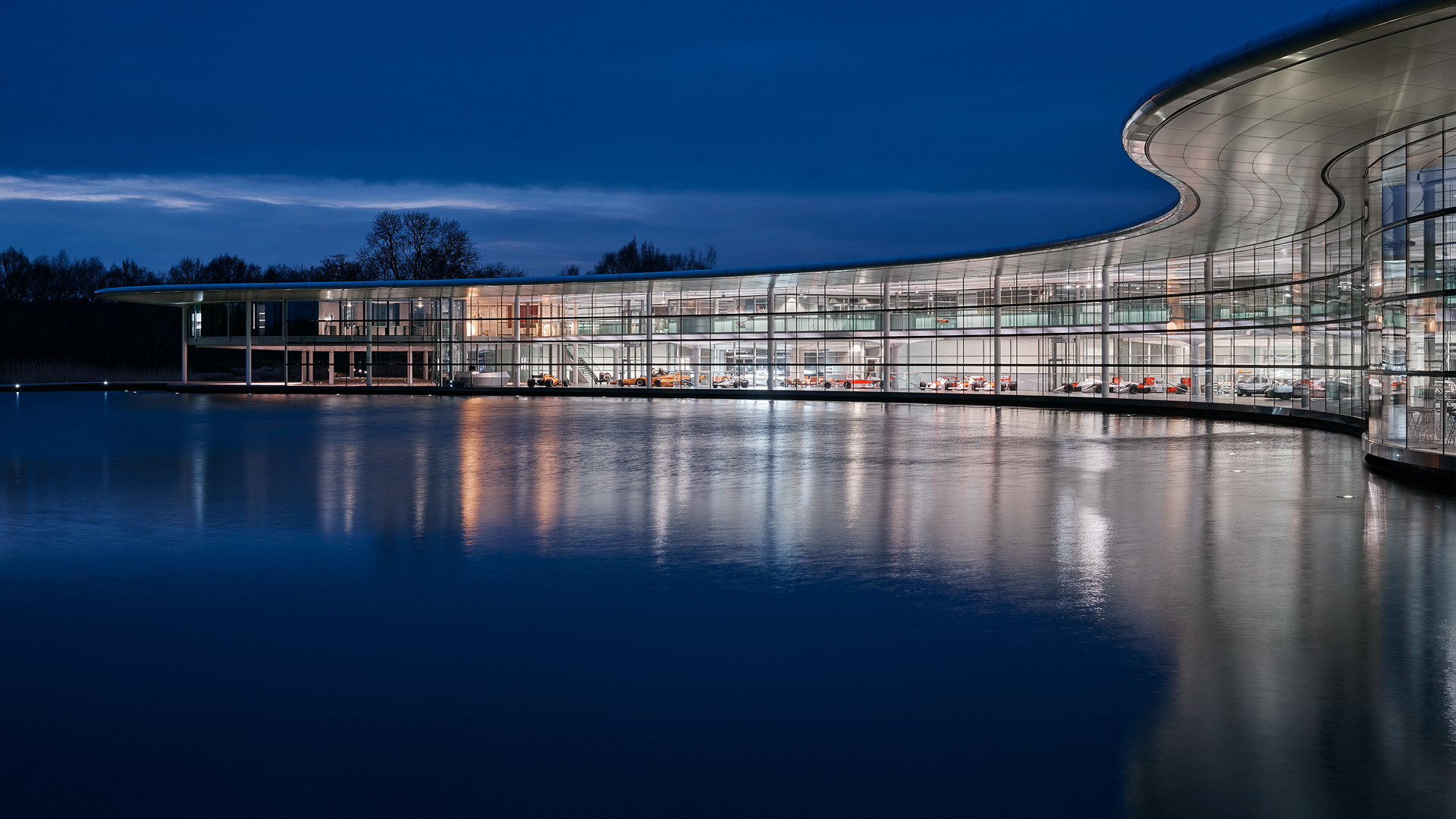 McLaren Technology Centre lit up at night, and reflected on the water front. 