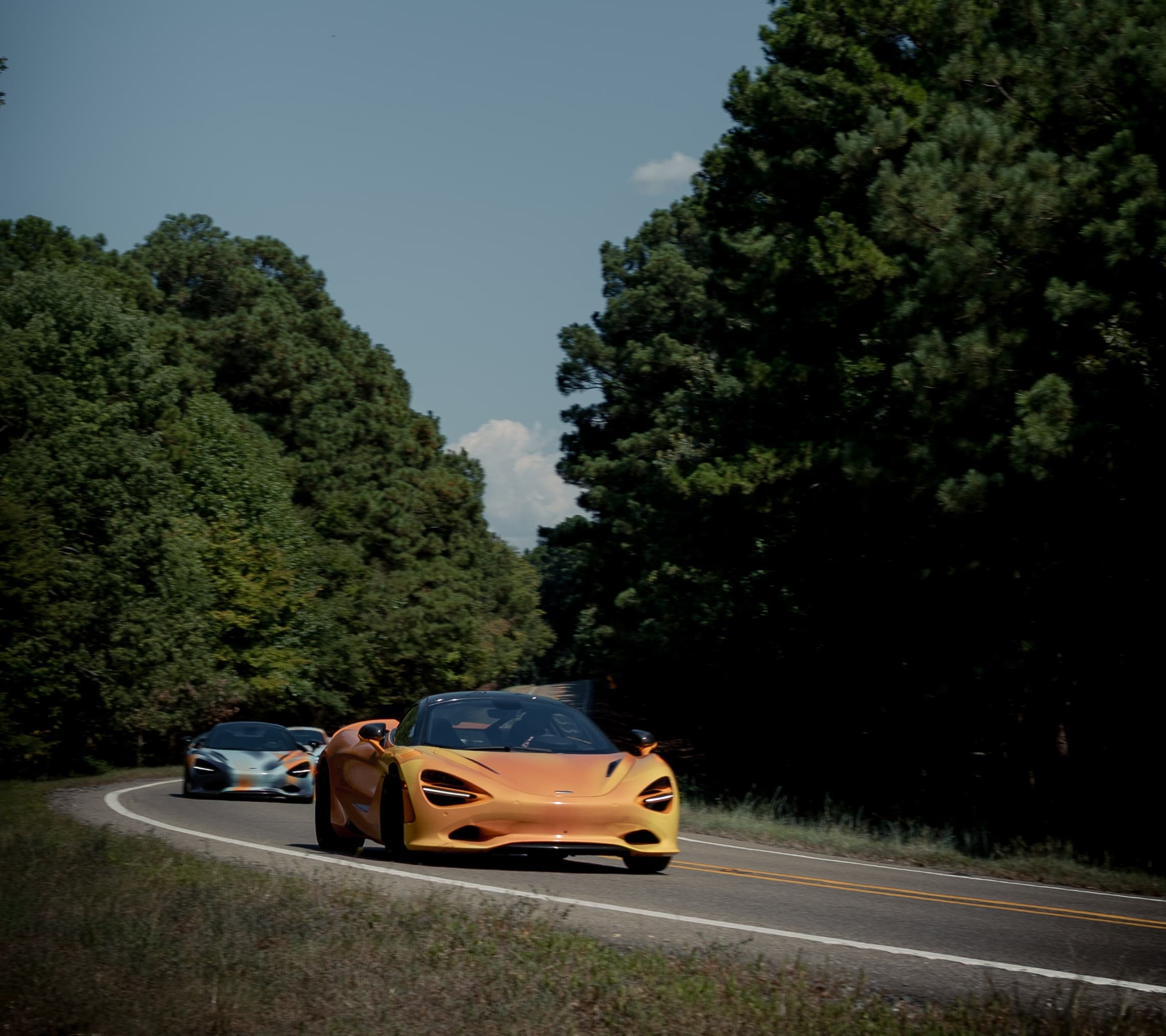 The States of Endurance McLarens driving around a bend, or a road surrounded by trees and greenery. A scene from Day 7 of the 'McLaren States of Endurance' road trip.