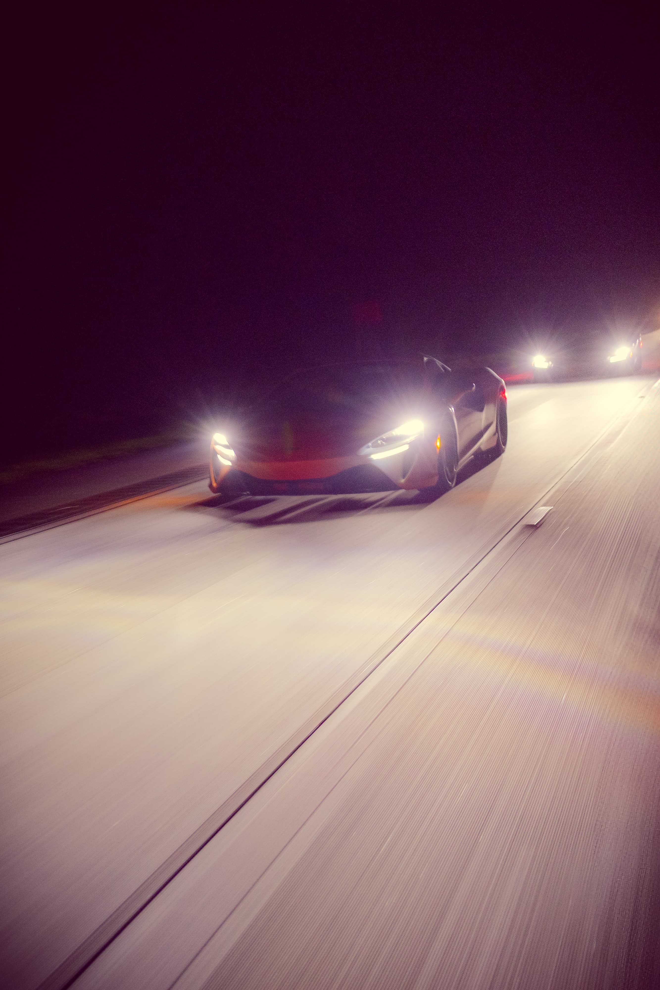 McLaren cars driving down the highway at night with headlights on. A scene from Day 9 of the 'McLaren States of Endurance' road trip. 