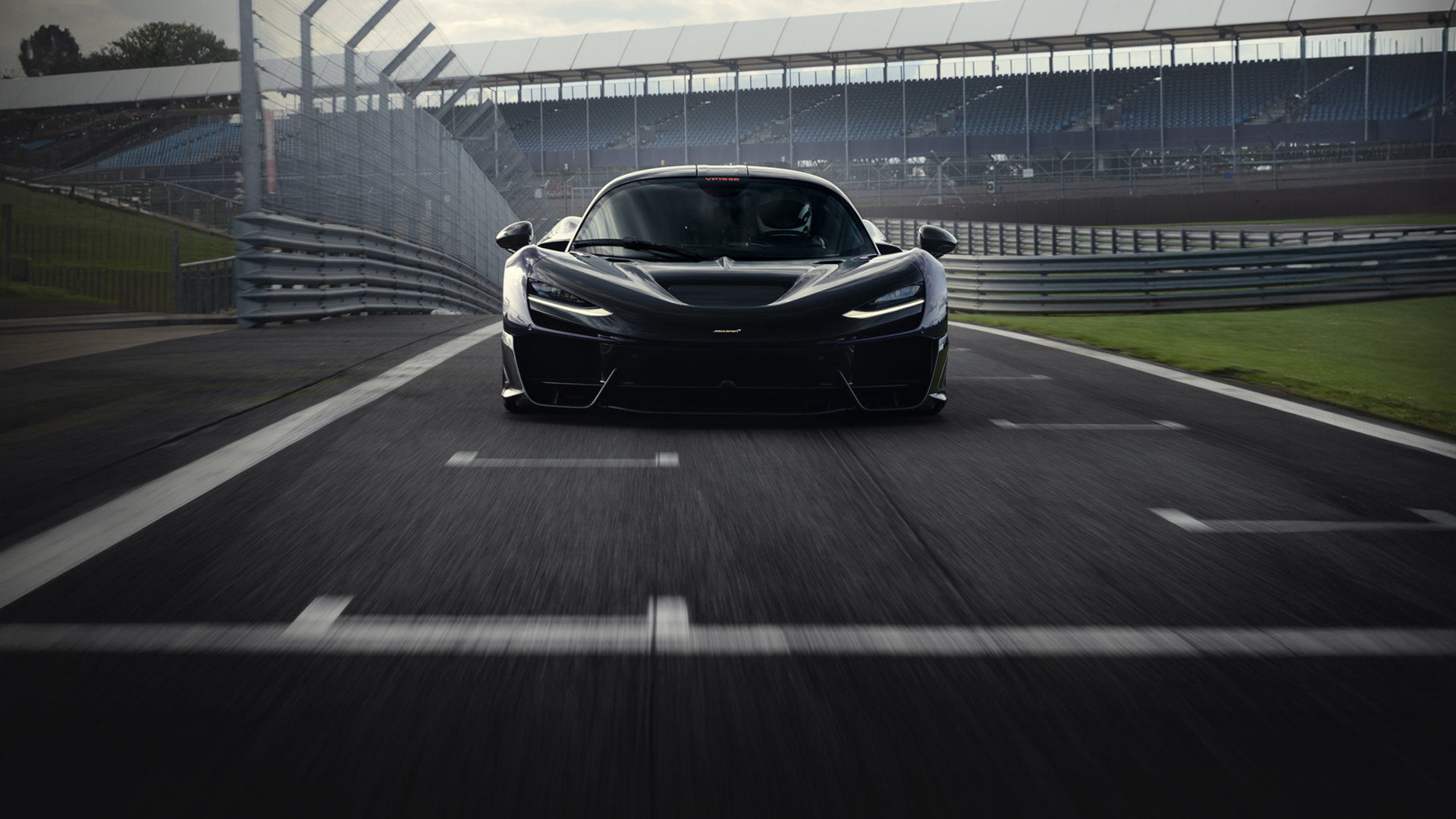  A low-angle view of the McLaren W1 hypercar on the iconic Silverstone Circuit, representing the brand's racing legacy.
