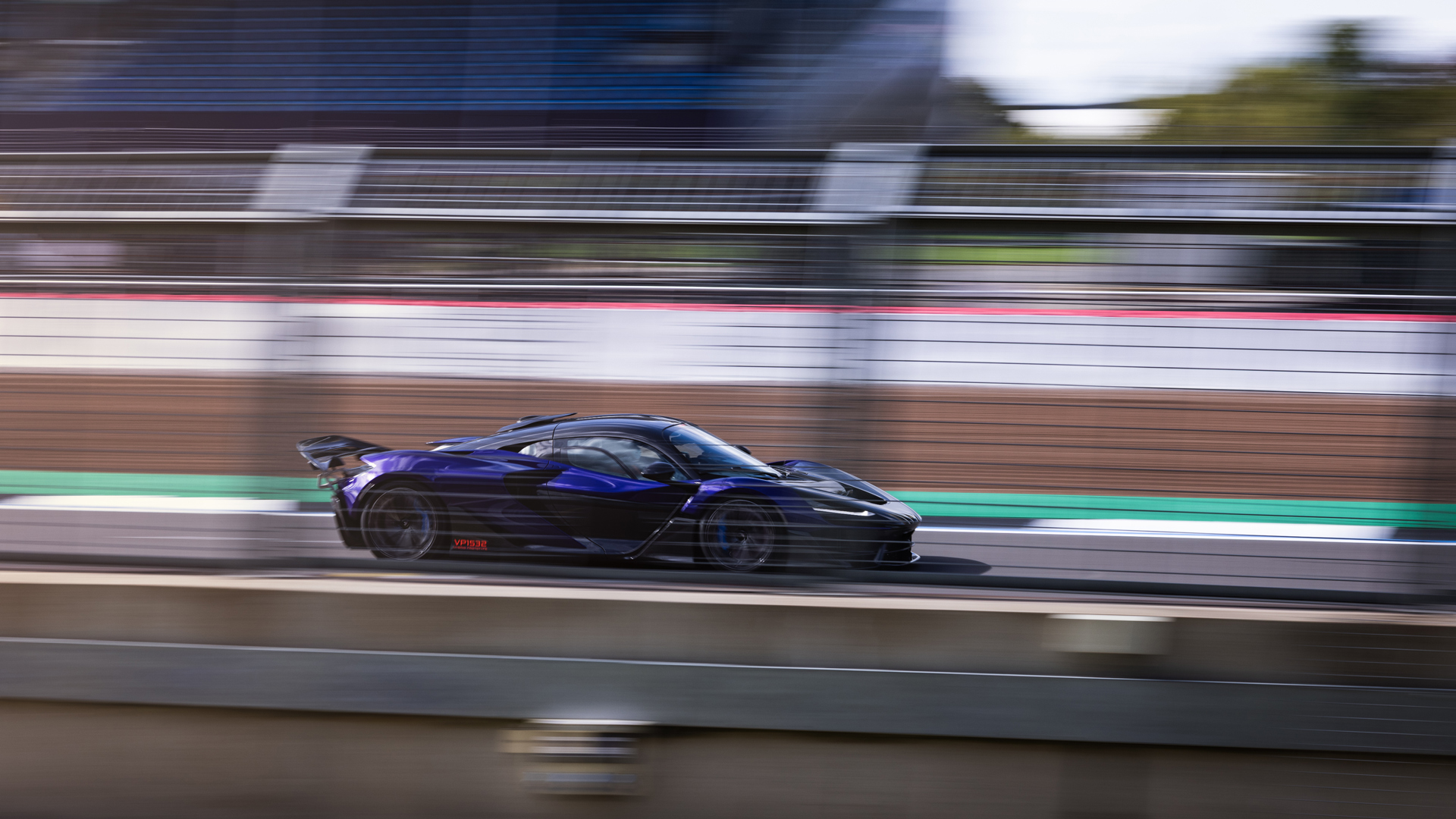 A shot of the side of a McLaren W1 prototype in royal blue driving at speed around the Silverstone track with motion blur to enhance the idea of speed.