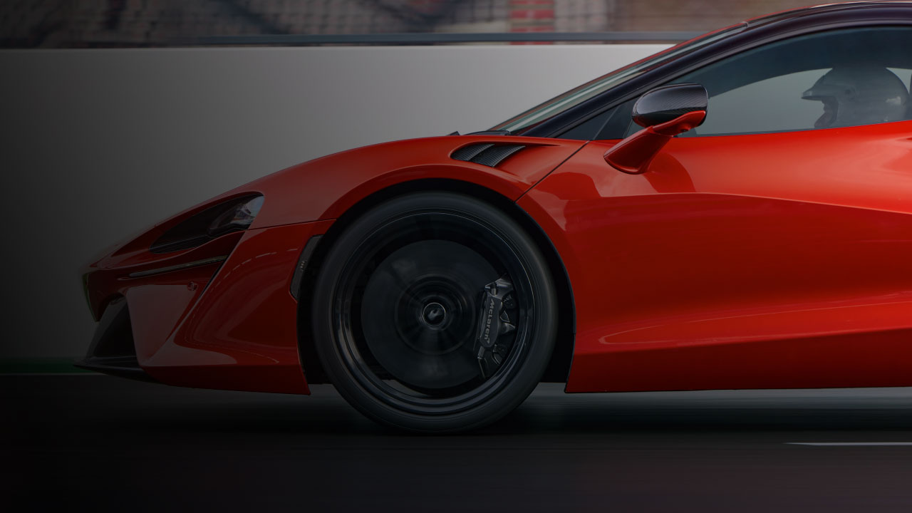 Close up side profile of a red McLaren 720S, driving on a race track.