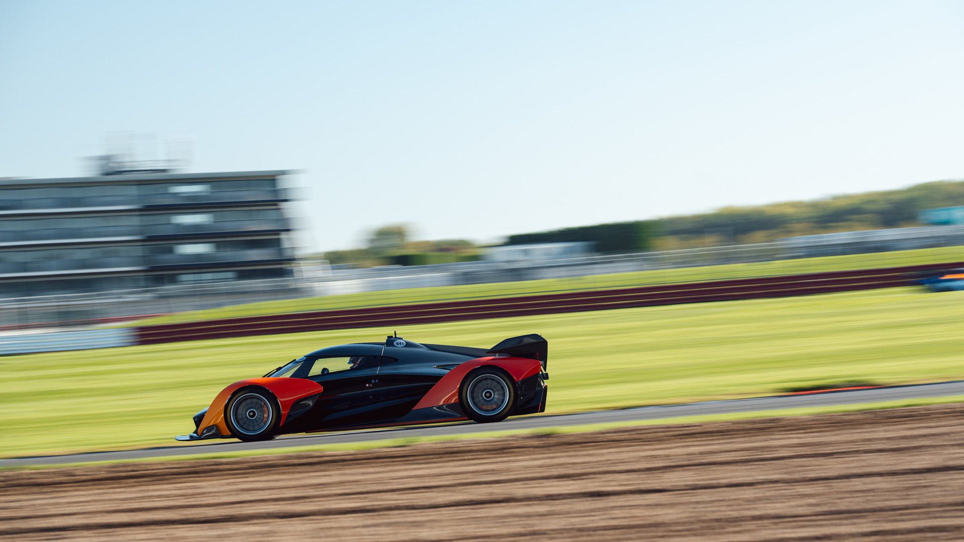 A side on shot of the McLaren Solus GT driving at speed along the Silverstone track. The motion blur emphasises the fast paced motion of the supercar.