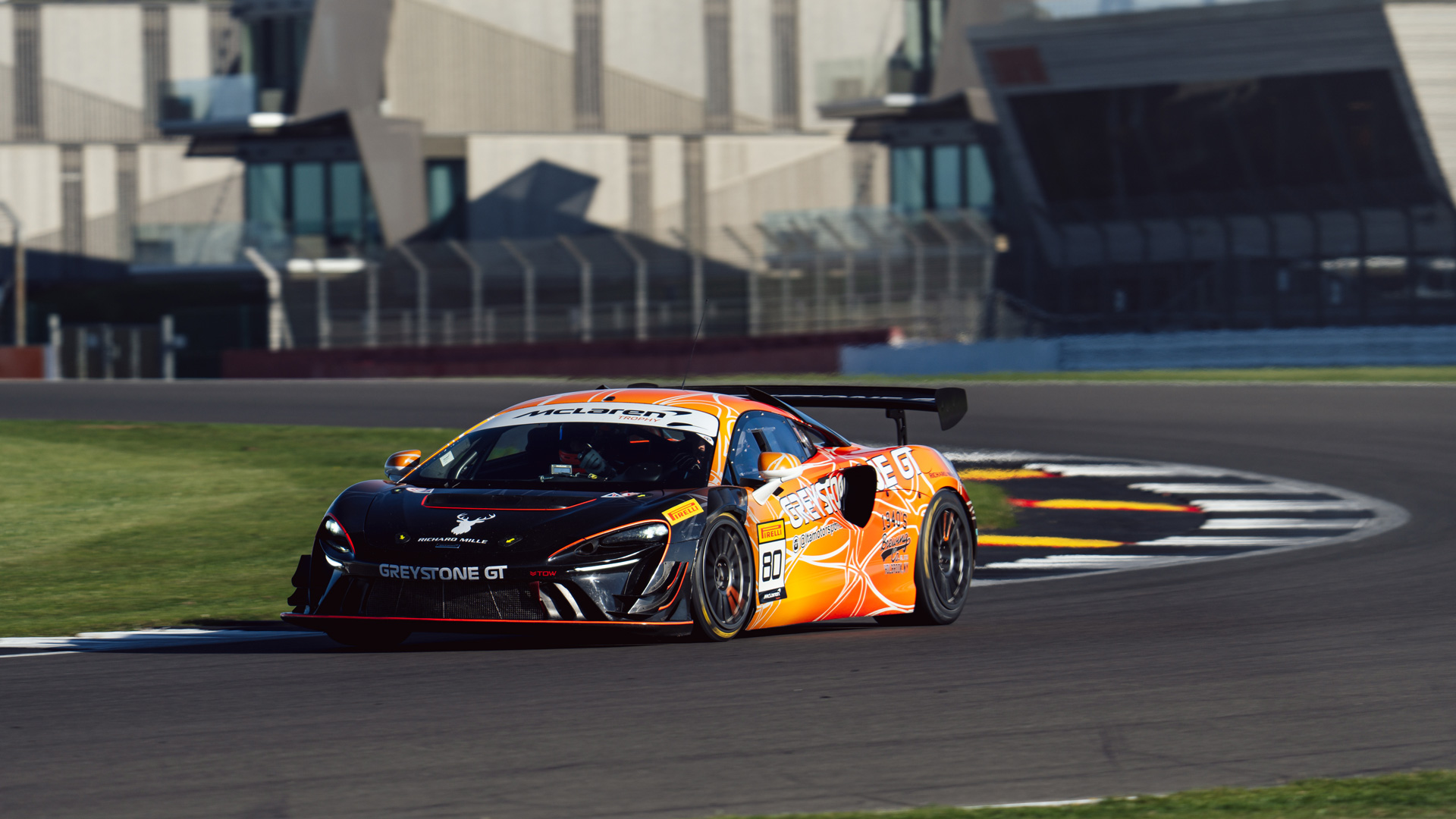 The McLaren GT with Greystone livery driving around a bend on a race track.