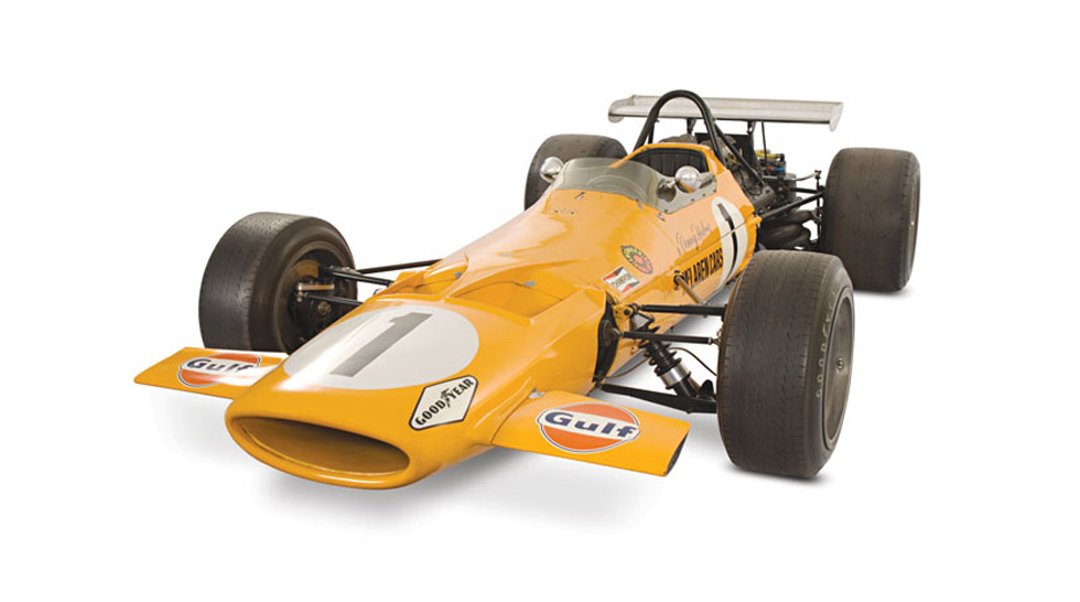 Front side view of the orange McLaren M7A, covered in sponsorship stickers and the number 1 painted onto its body. Photographed on a white background.