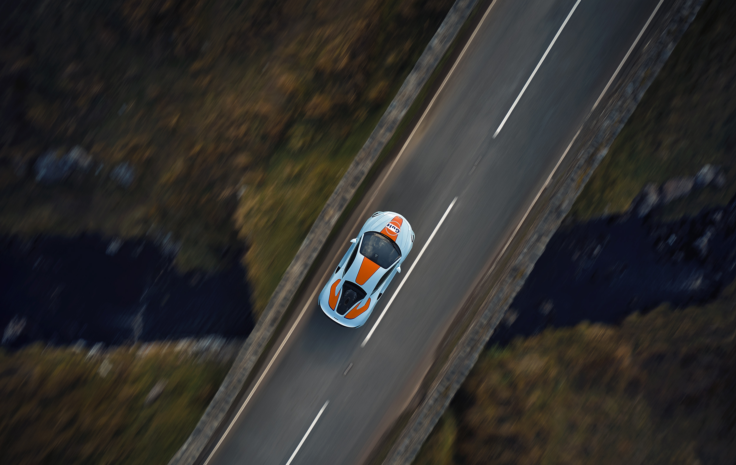 Top view of Gulf branded McLaren, driving over a bridge at speed. 