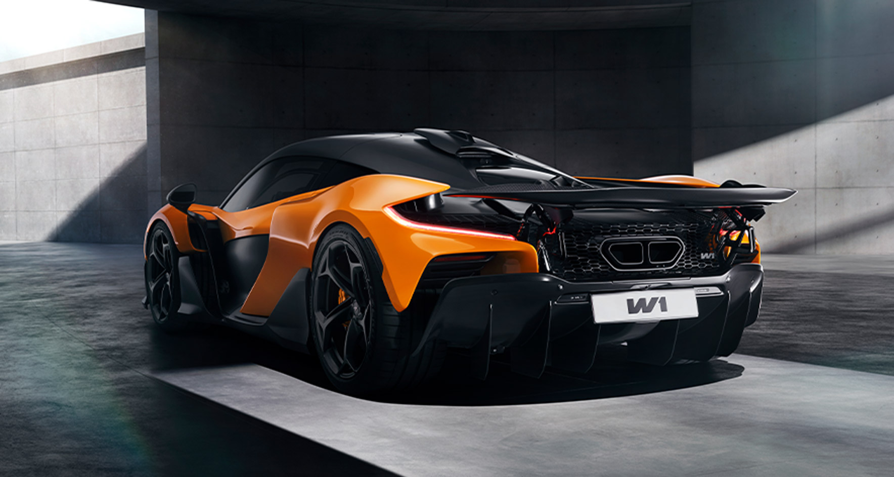 A low, rear three-quarter view of the orange McLaren W1 showcasing its aggressive diffuser and intricate rear design against a concrete backdrop.