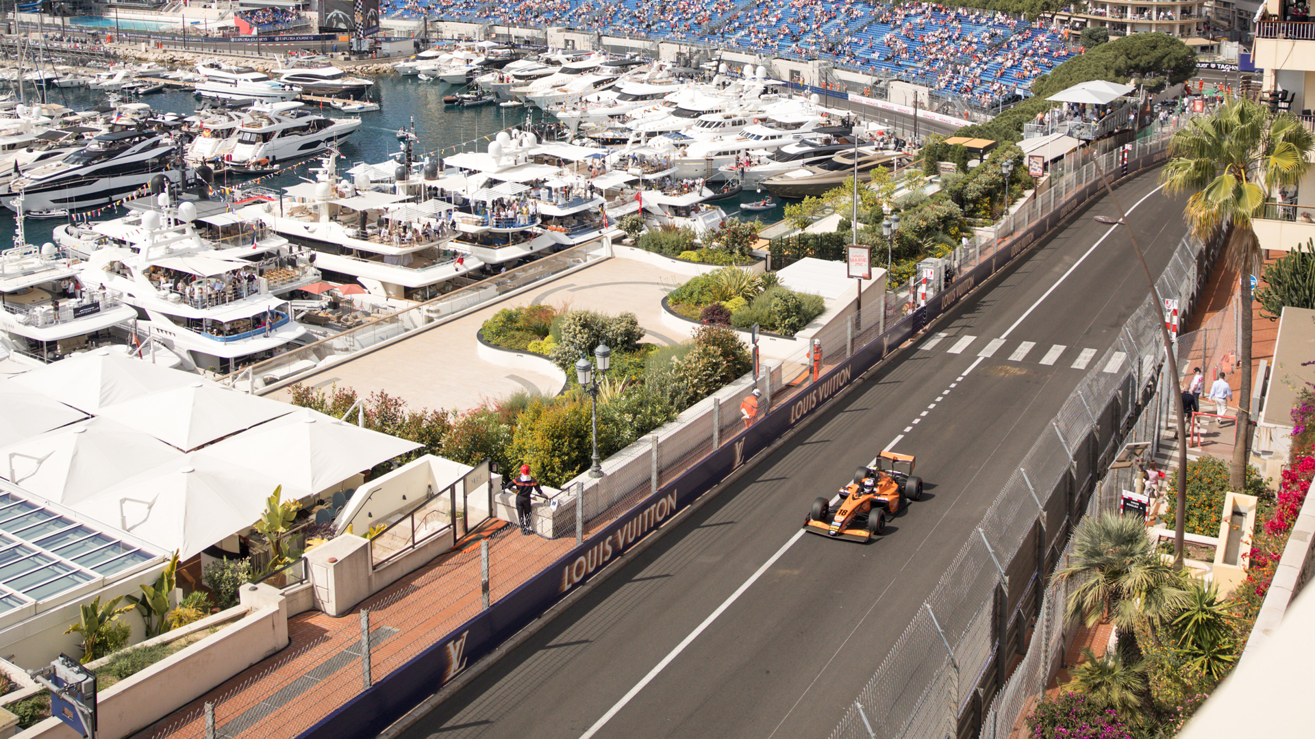McLaren Formula 1 car driving on the iconic Monaco Grand Prix street circuit track, showcasing the luxurious view from an exclusive McLaren F1 hospitality suite overlooking the harbor.