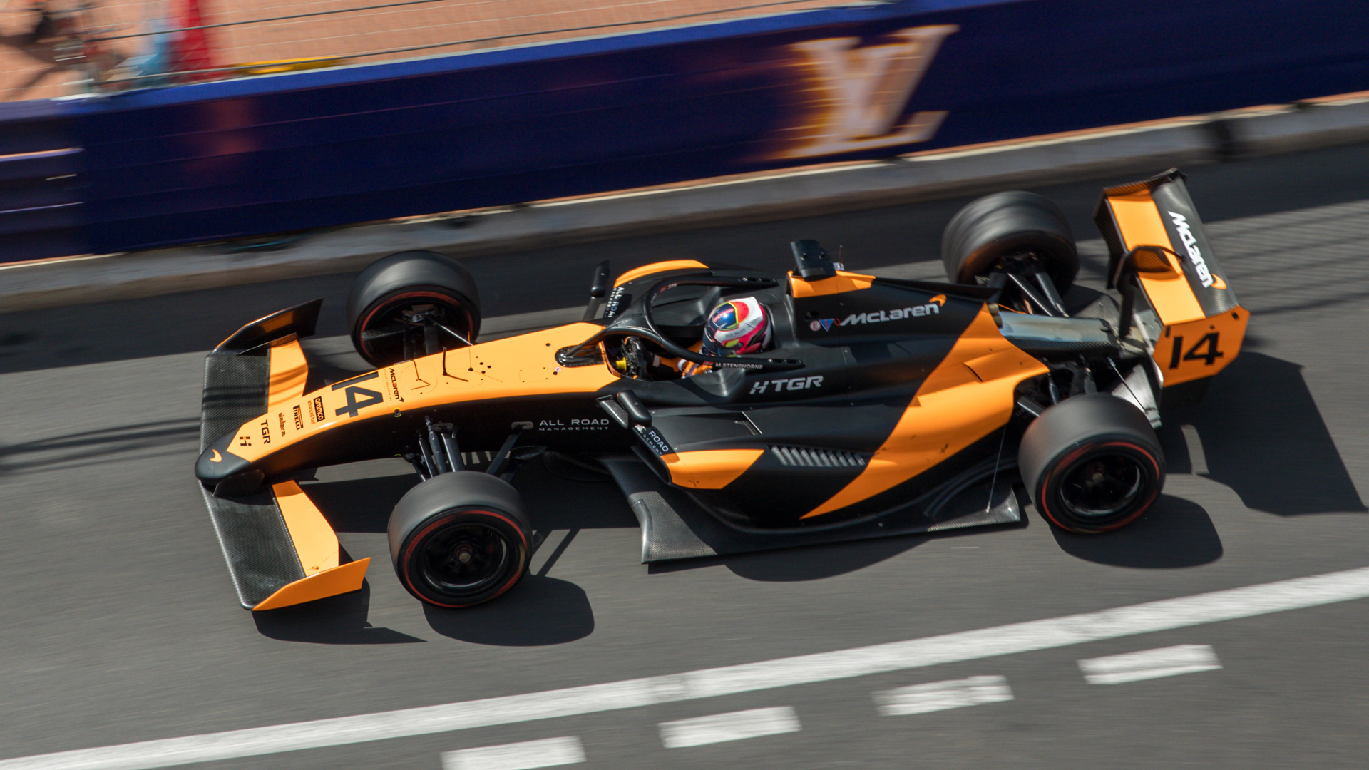 Overhead shot of a McLaren F1 car speeding on the iconic Monaco Grand Prix street circuit, demonstrating the high-speed action that guests witness from the exclusive McLaren F1 hospitality viewing areas.