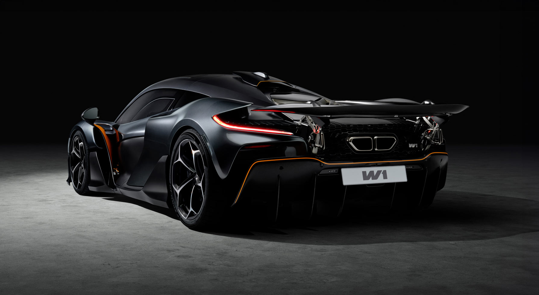 A rear view of the black McLaren W1 illuminated by a spotlight, highlighting its complex rear end with active aero and prominent exhaust outlets.