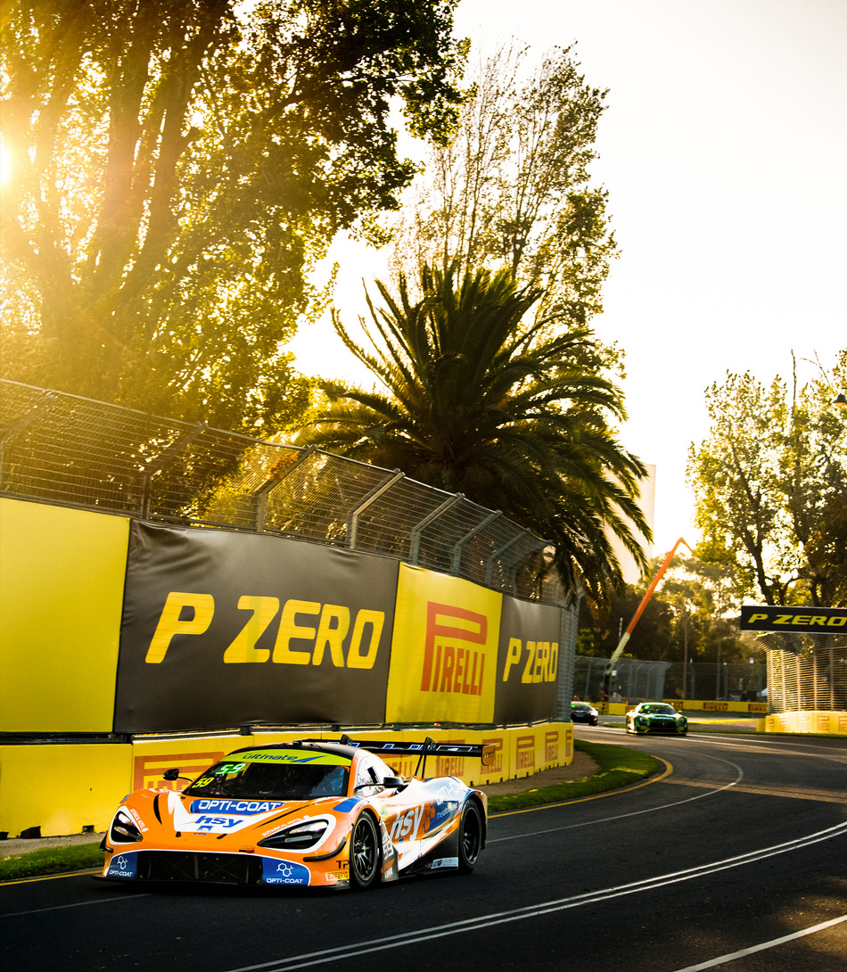 A McLaren Racing 720S GT3 driving around a race track, with a wall covered in Pirelli P Zero sponsorship in the background.