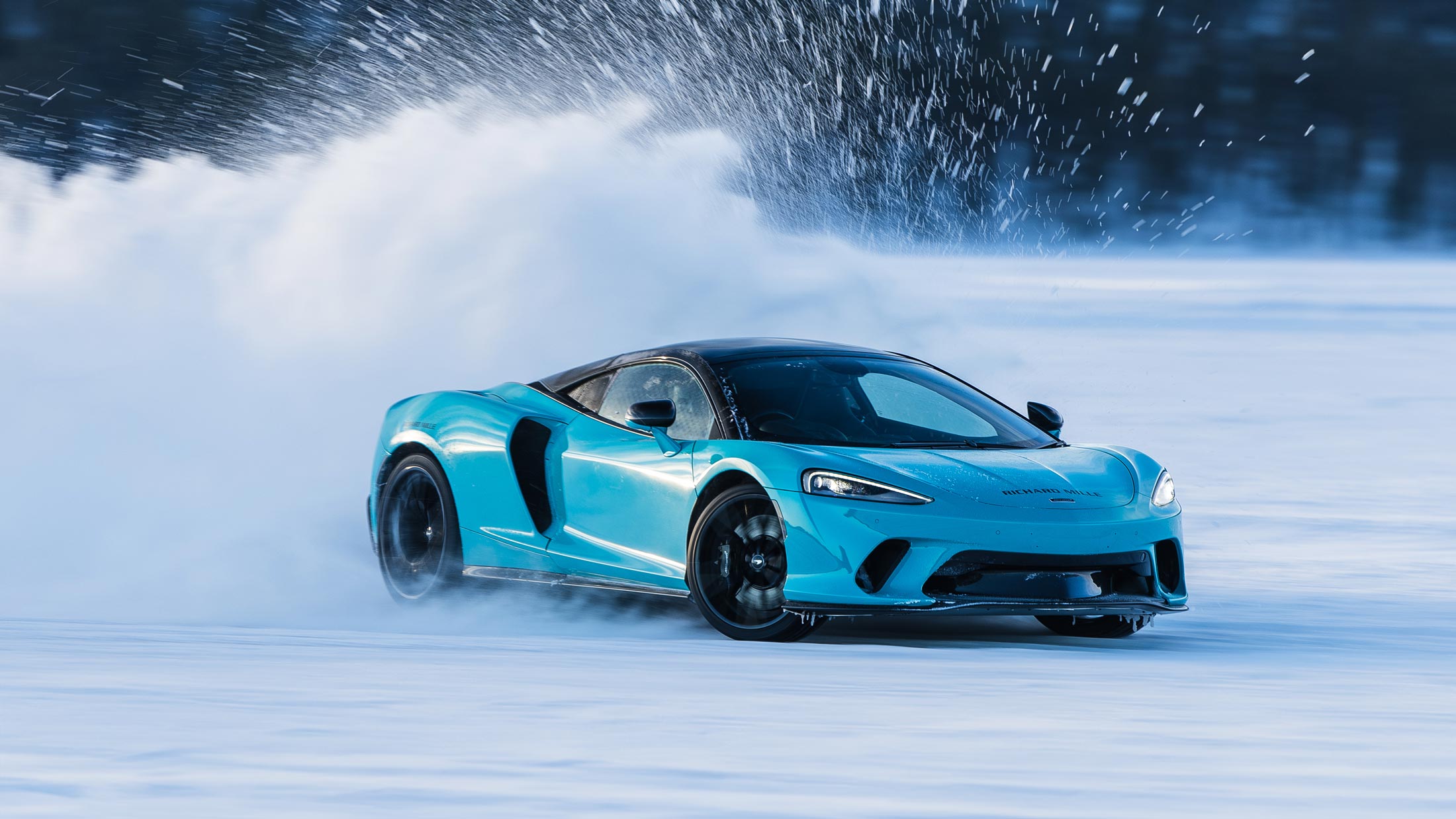 Black McLaren supercar driving sideways on a frozen lake at sunset, showcasing the thrilling Pure McLaren Arctic Experience ice driving event.