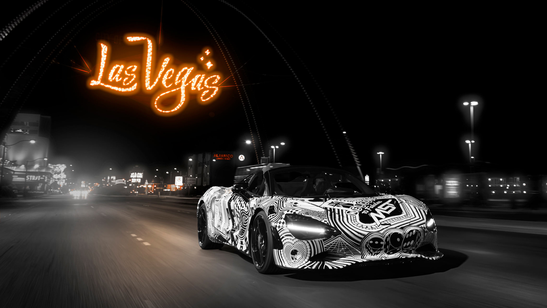 The McLaren 750S Spider 'Project Viva' driving at night on a Las Vegas road, with a stylized neon orange 'Las Vegas' sign digitally integrated above, emphasizing the MSO car's theme.