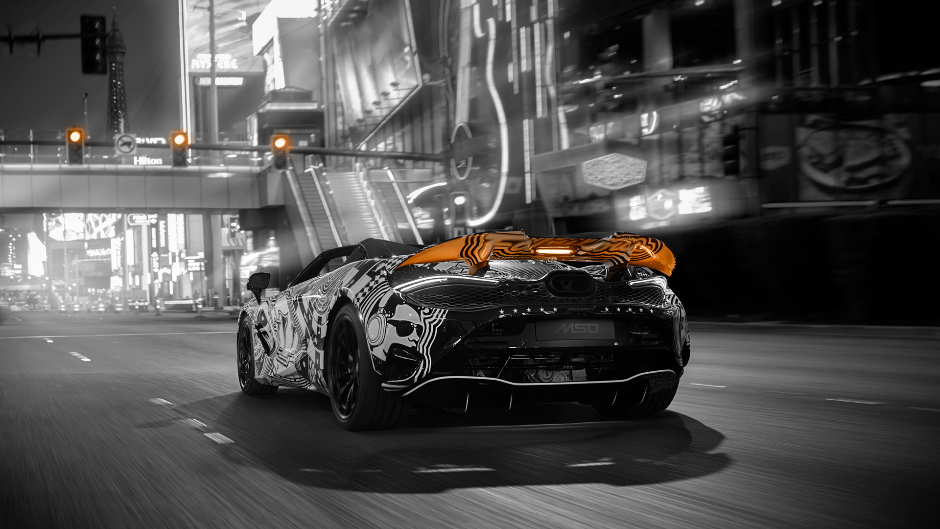 ear view of the MSO Project Viva driving in a Las Vegas street scene, highlighting the hand-painted, McLaren orange glow highlighting the rear wing and the bespoke MSO designation.