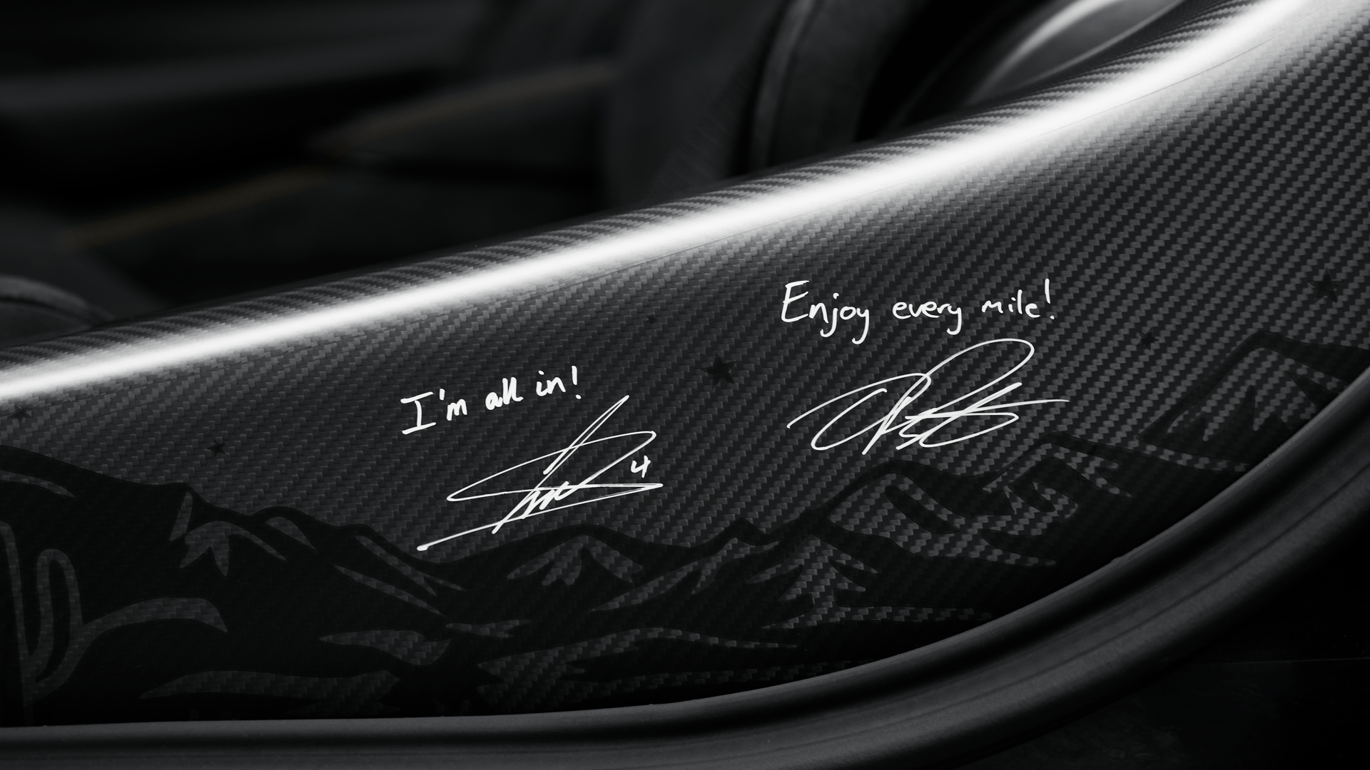Close-up of the custom carbon fibre interior trim on the McLaren 750S MSO featuring engraved signatures from McLaren F1 drivers Lando Norris and Oscar Piastri, reading 'I'm all in!' and 'Enjoy every mile!'.